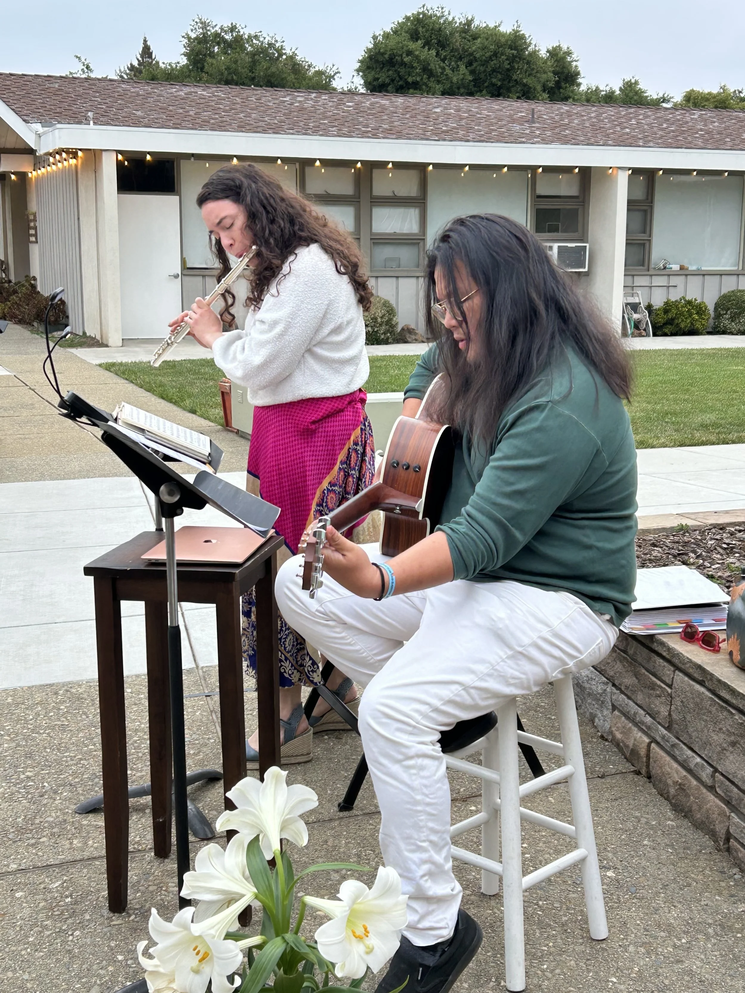 A man and a woman playing the guitar and the flute outdoors on the patio during a worship service
