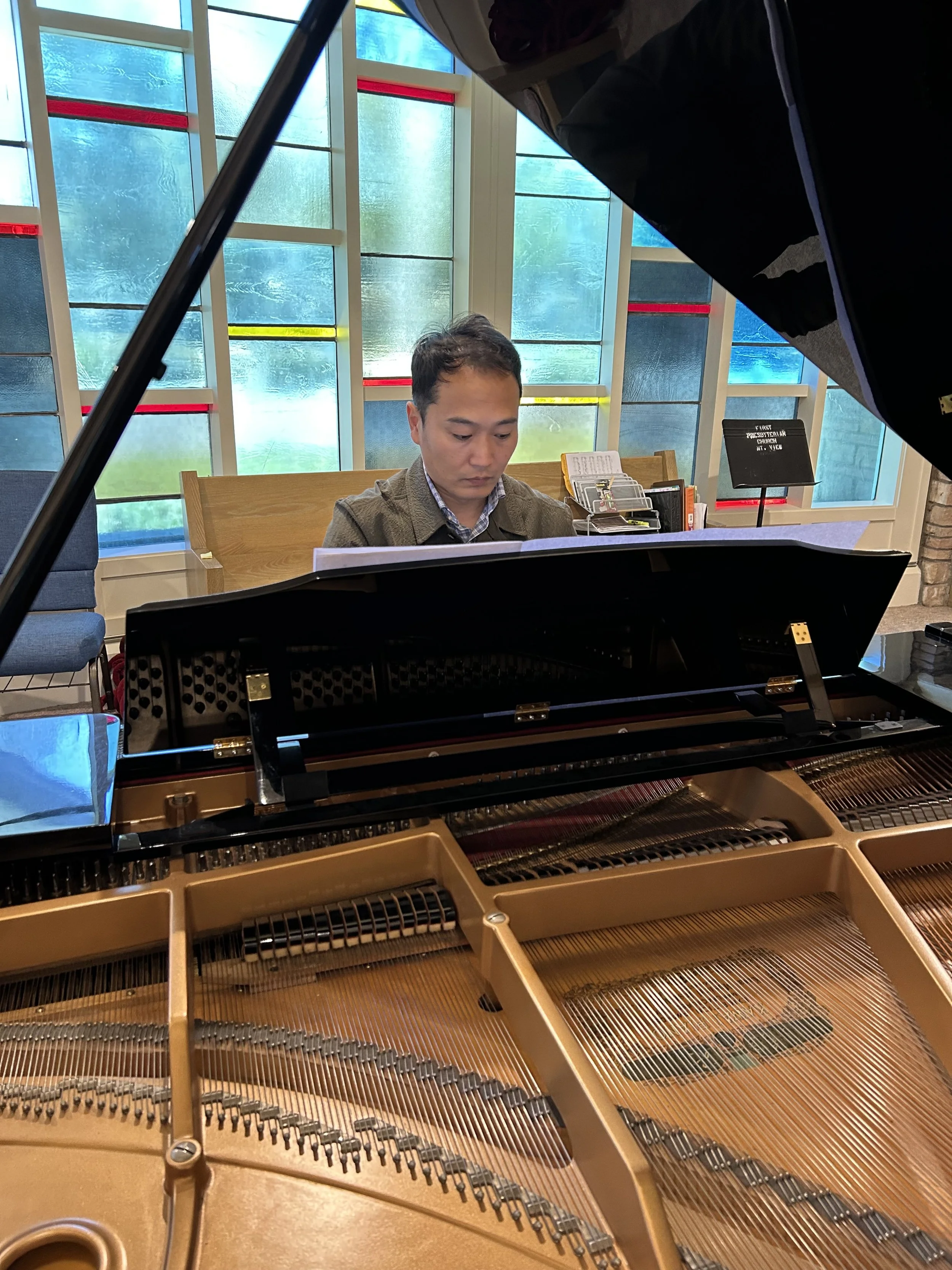 a man at the piano in front of a wall of stained glass windows in the church sanctuary