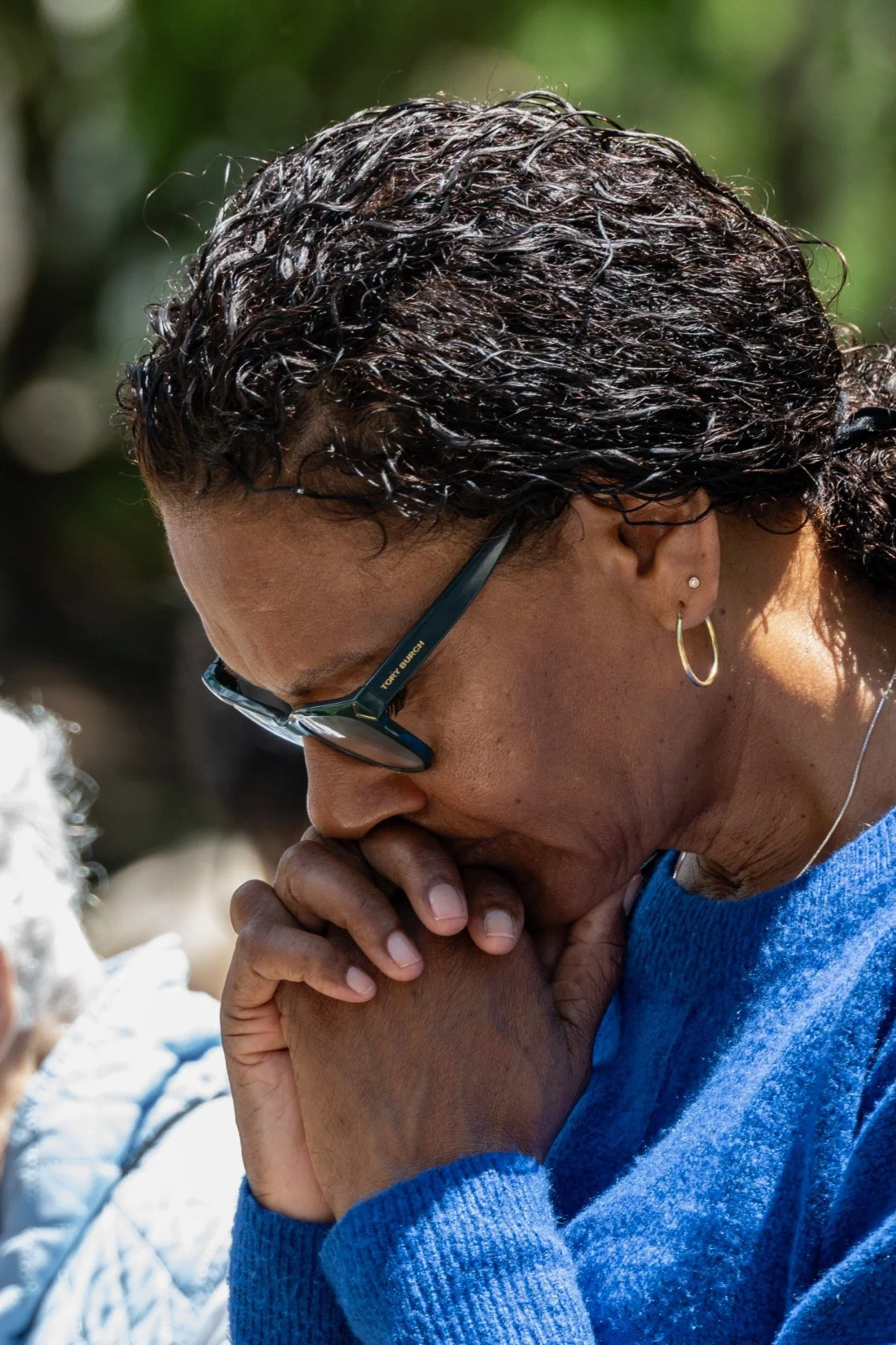 a woman wearing sunglasses bows her head in prayer