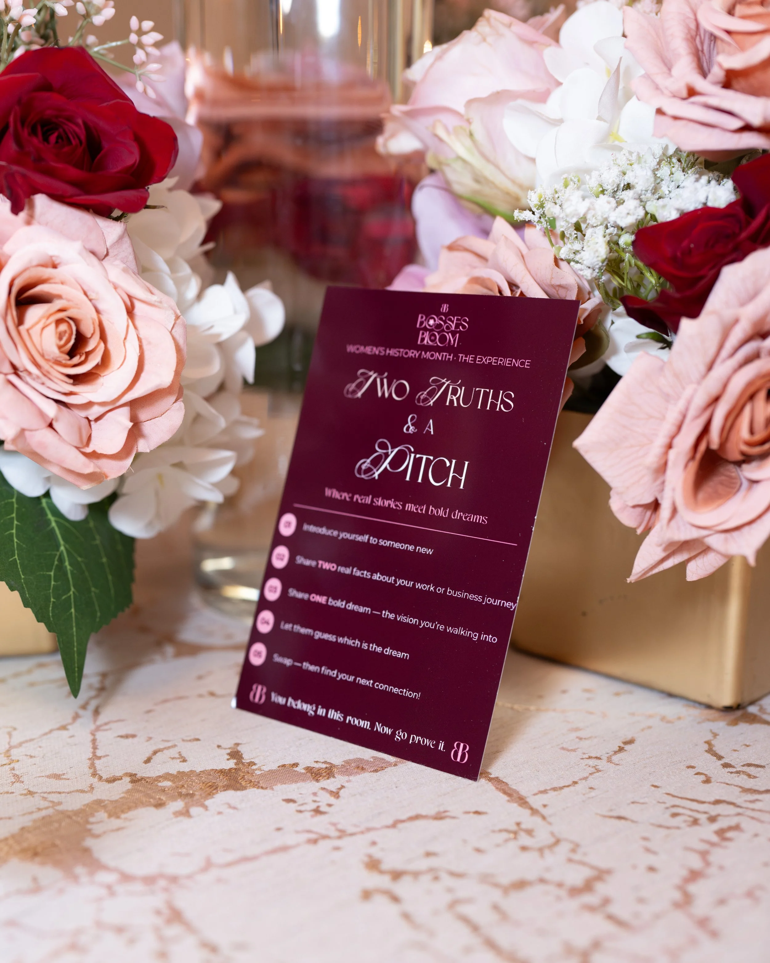 Close-up of a floral arrangement with red, pink, and white roses and other flowers, along with a burgundy flyer or card with text.