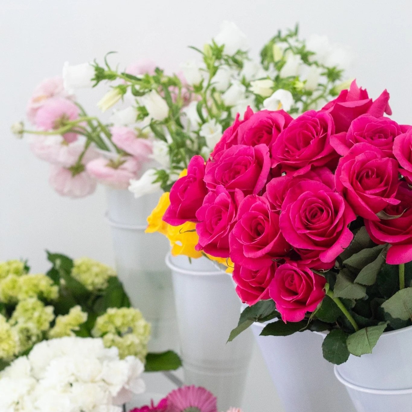 Arrangement of pink, white, yellow, and green flowers in white vases on a white surface.