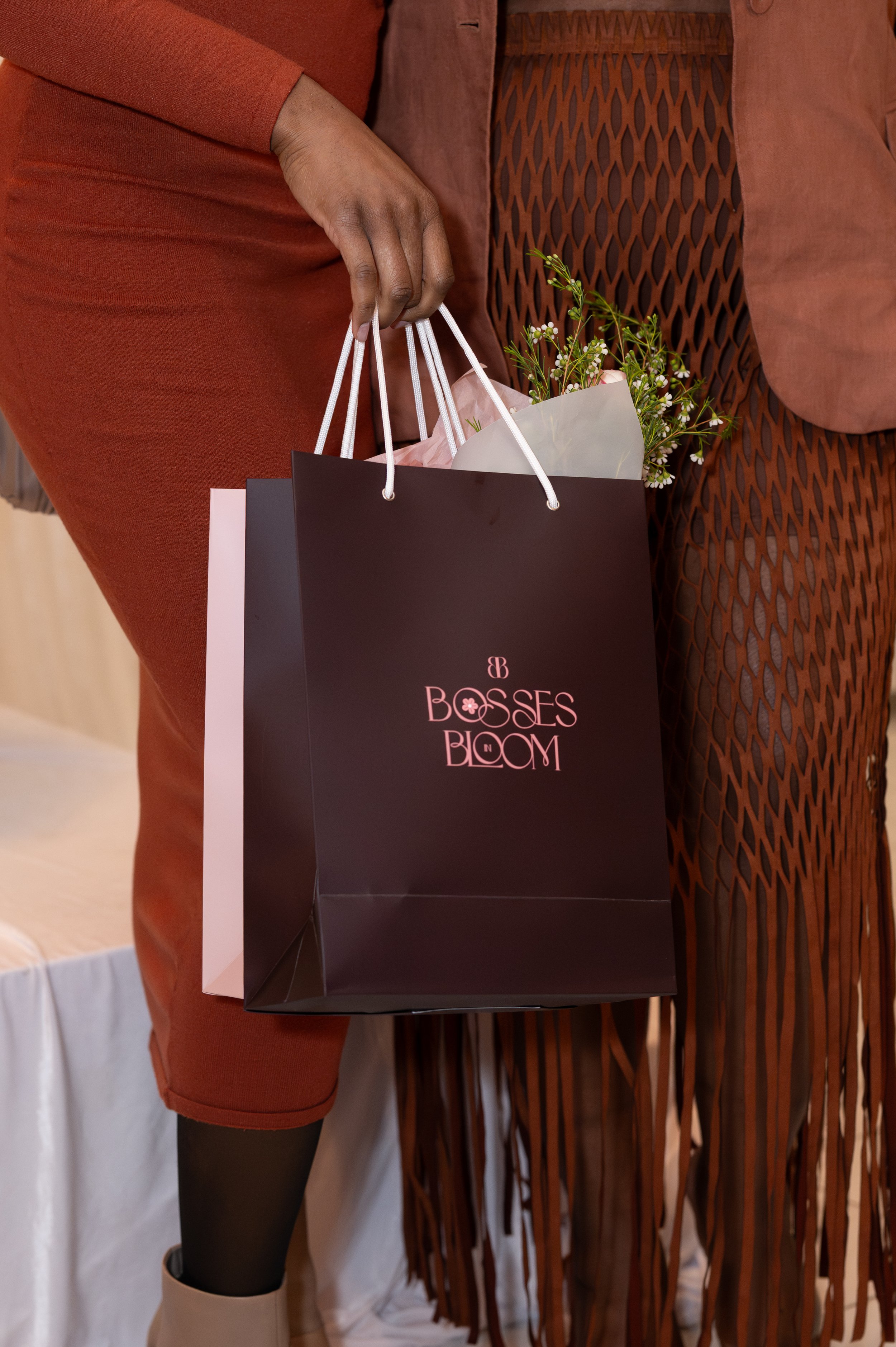 Person holding a black gift bag with pink writing, with small flowers and pink tissue paper inside.