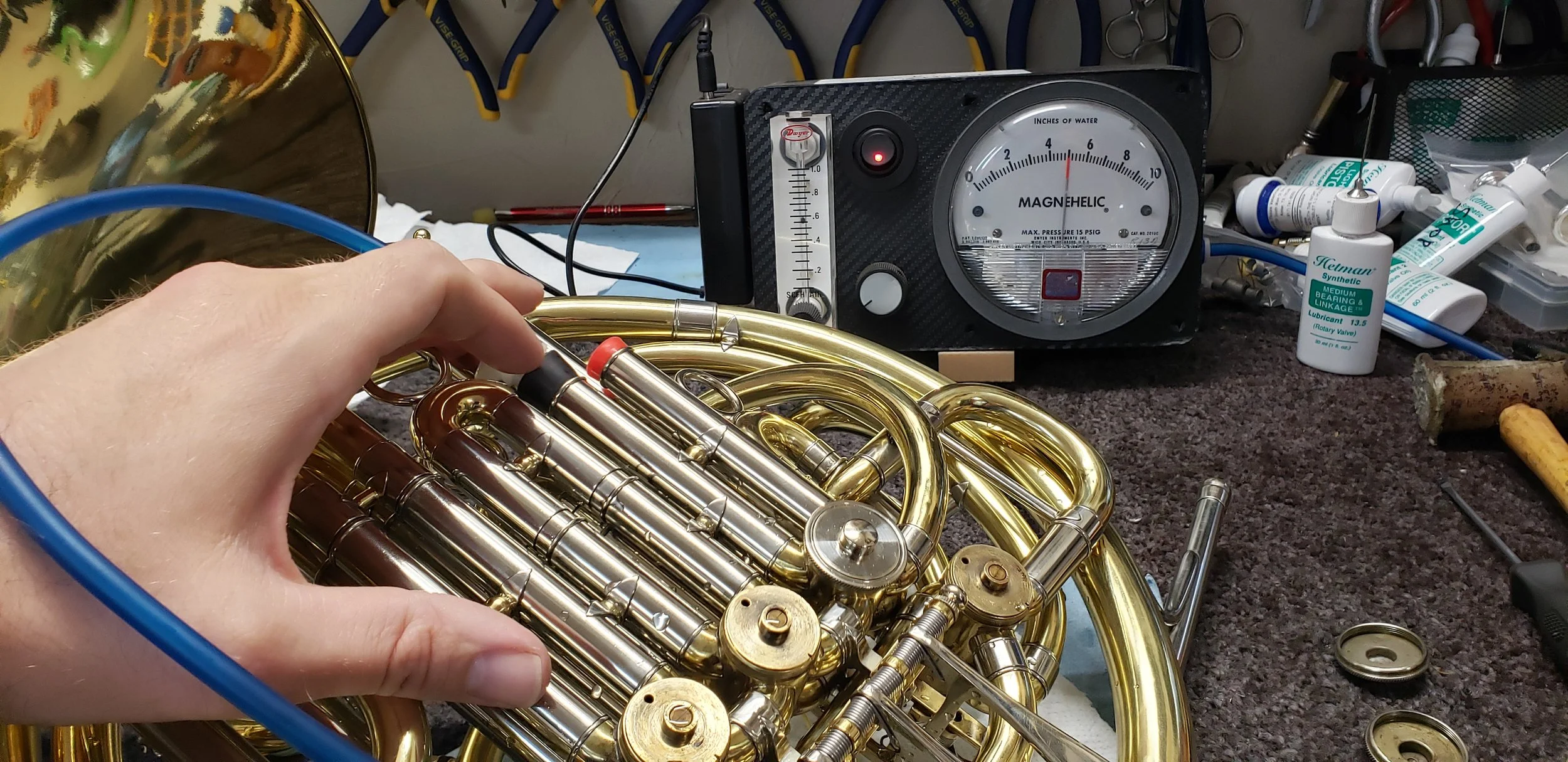 Testing rotor compression on a Holton double French horn using a Magnehelic gauge and Leak Pro during initial diagnostic assessment.