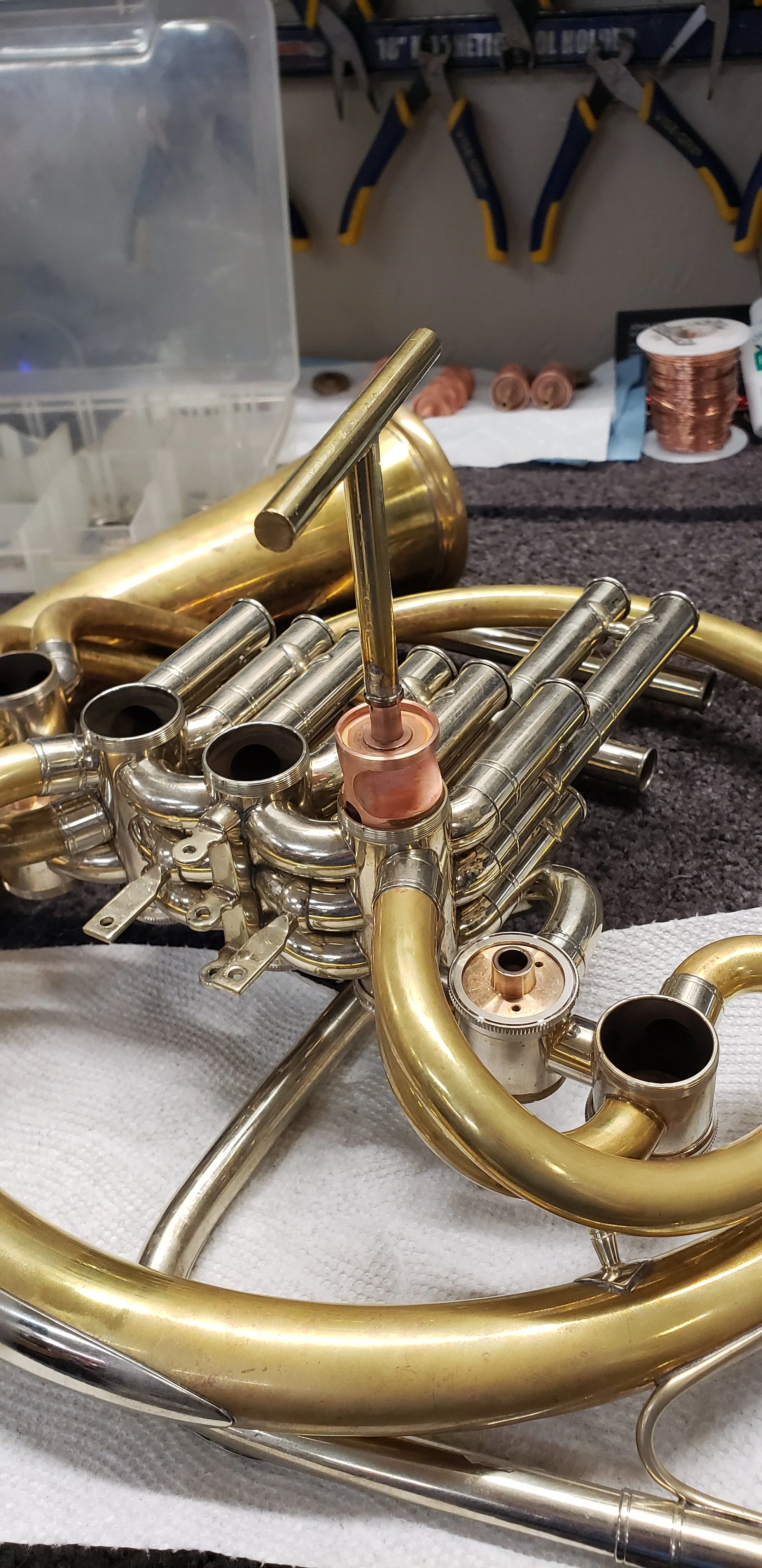 A Schmid Triple French Horn with a copper plated rotor with a custom lapping handle sitting halfway in the valve casing.