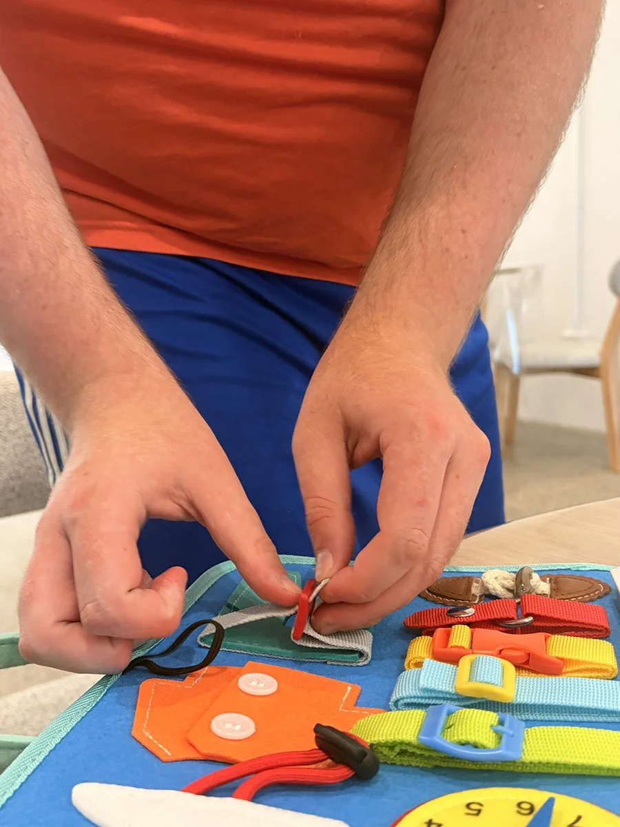 Person's hands organizing colorful pet collar tags and accessories on a blue mat.