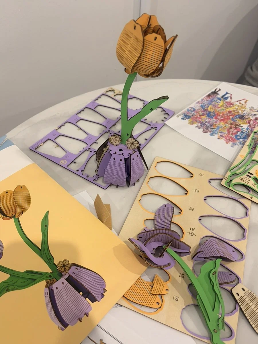 Various colorful paper and wooden cutouts of flowers and stems for crafting, arranged on a table.