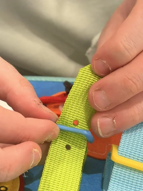 Close-up of two hands attaching a yellow buckle strap to a blue strap on a colorful item.