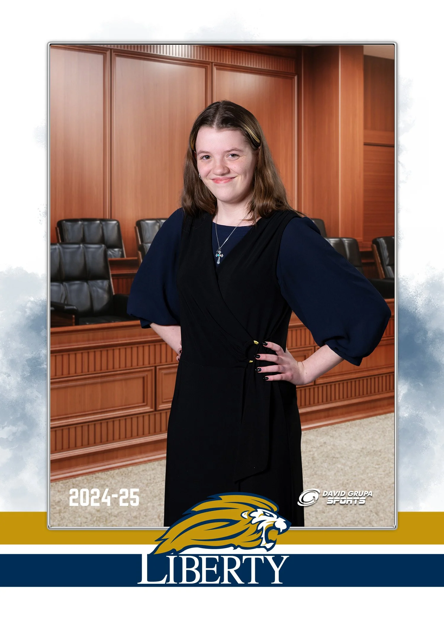 Young girl standing confidently in a courtroom setting with wood paneling and empty black chairs behind her. She is wearing a dark dress with a blue top, a necklace with a cross, and has her hand on her hip. The image features the Liberty University 