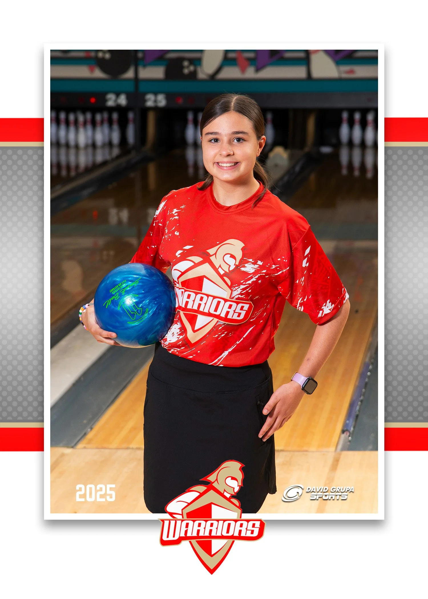 A young girl standing on a bowling alley lane, holding a blue bowling ball with her right hand, wearing a red sports jersey with the word 'Warriors' and a warrior logo, a black skirt, and a smartwatch on her left wrist. She is smiling and has brown h