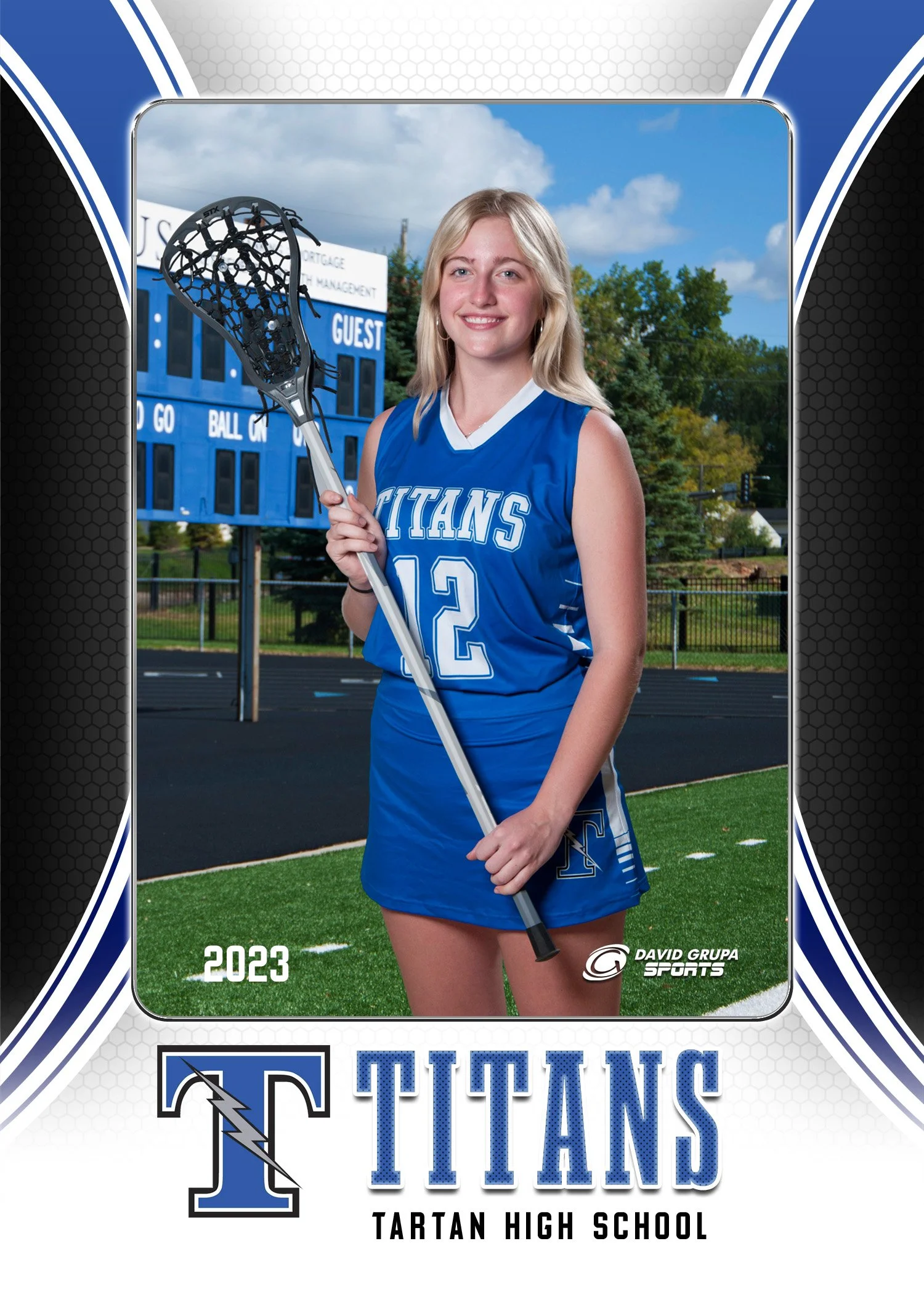 A young woman in a blue sports uniform holding a lacrosse stick on a high school sports field, with a scoreboard and trees in the background, celebrating her participation in Tartan High School lacrosse in 2023.