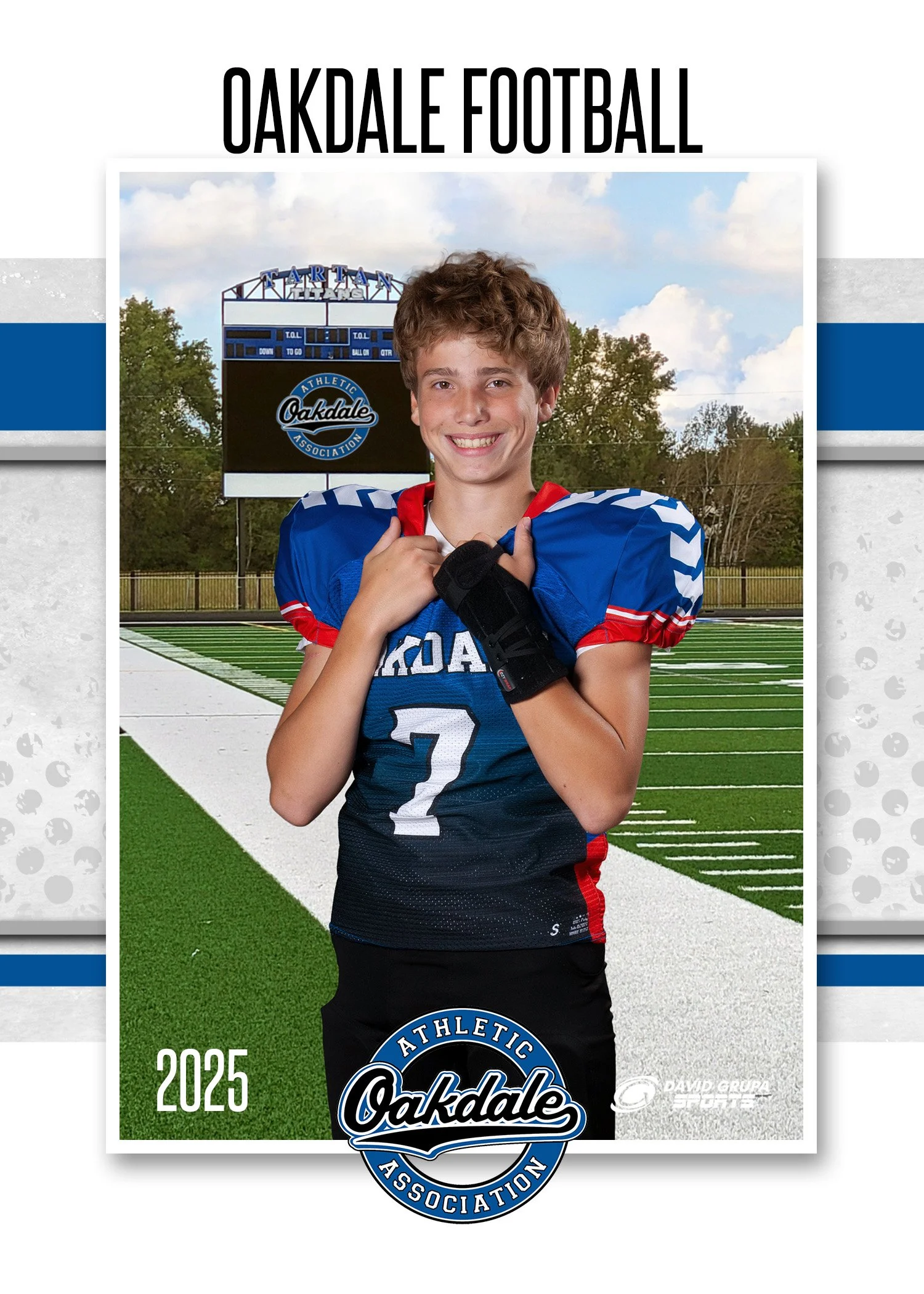 A young male football player in a blue and red jersey with the number 7 stands on a football field, holding his shoulder pads with both hands, smiling. In the background is a scoreboard and trees, with a cloudy sky overhead, and the text "OAKDALE FOO