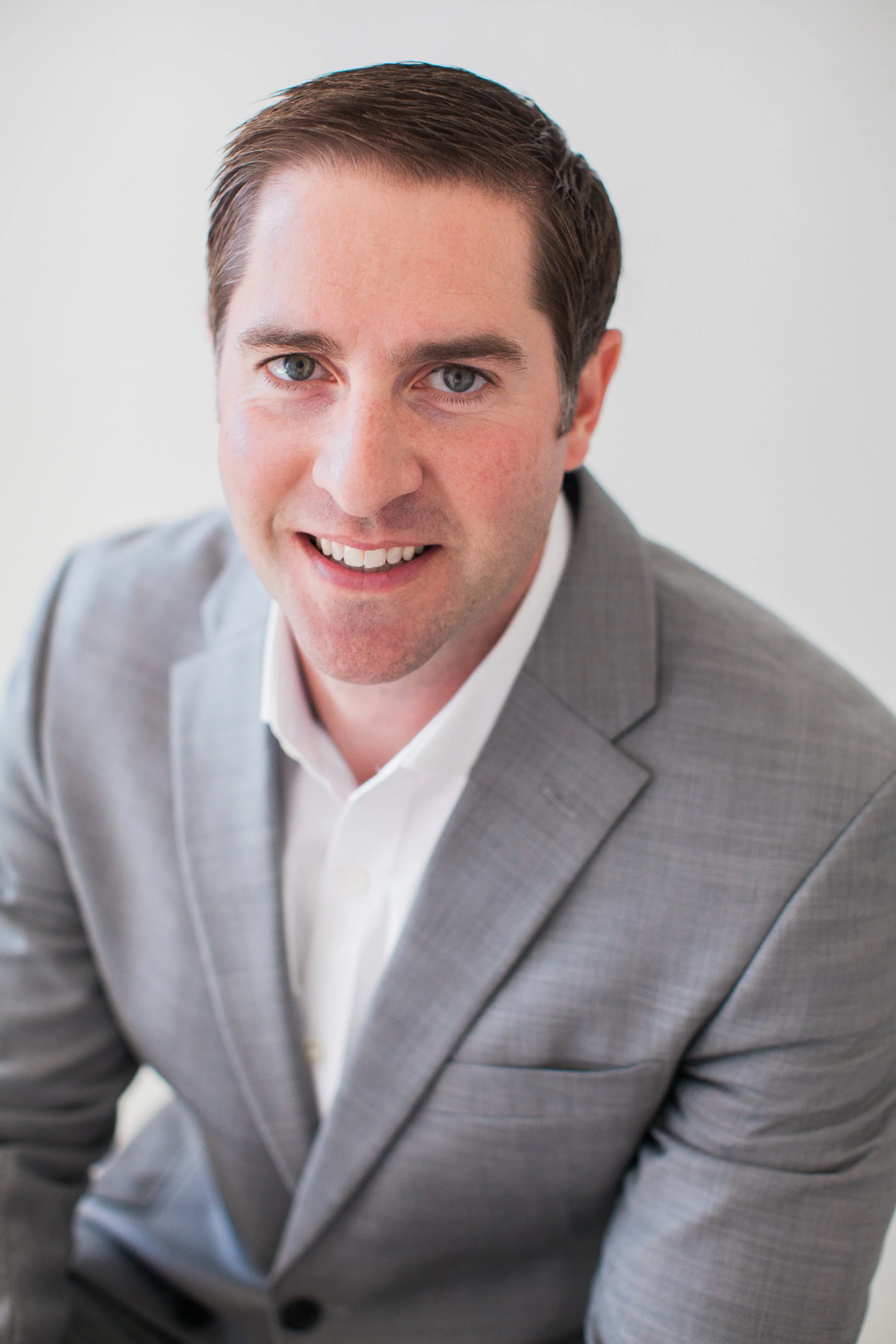 Close-up of a man wearing a gray suit and white shirt, smiling.