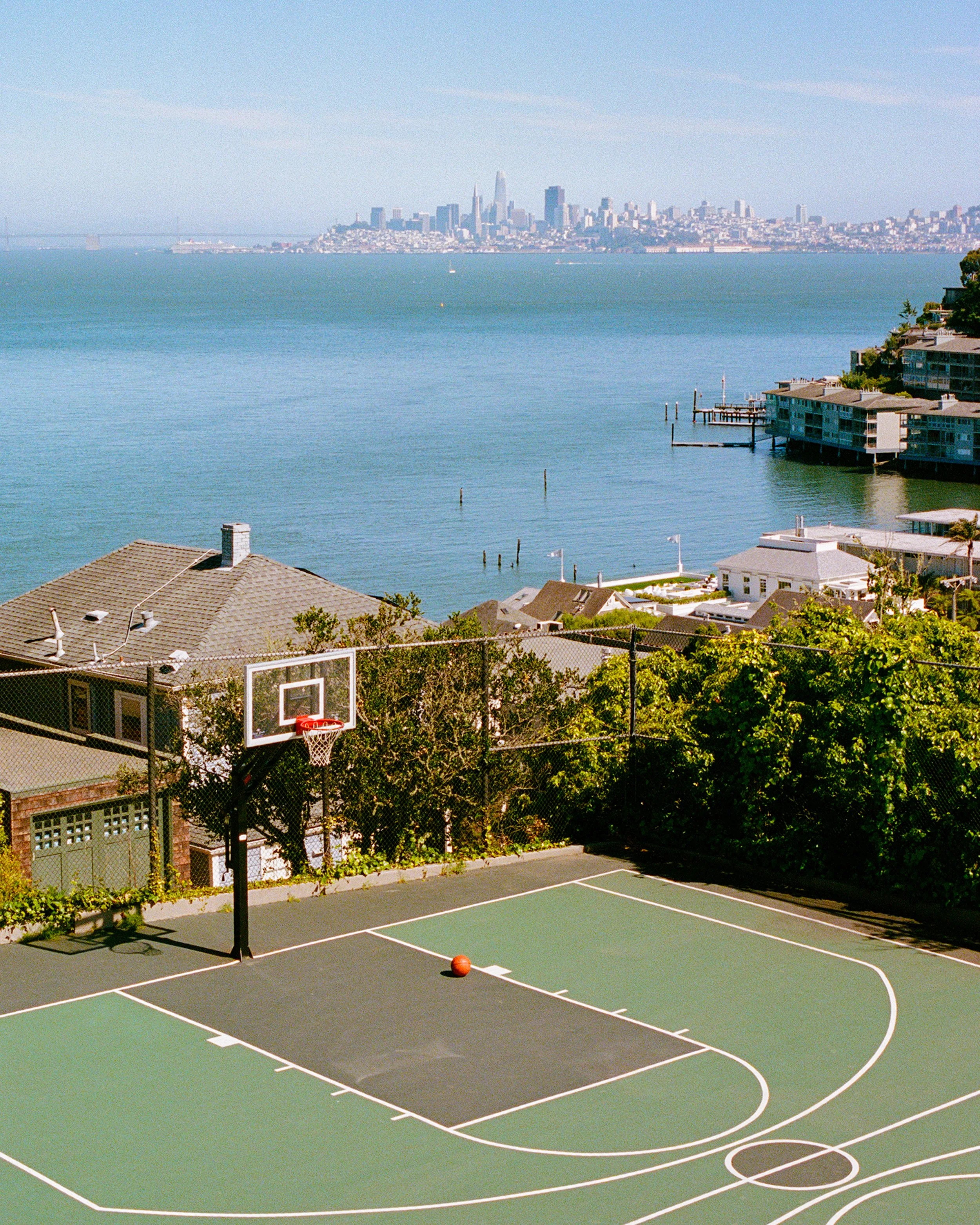 Basketball court overlooking the bay with a ball on the court and city skyline in the distance.