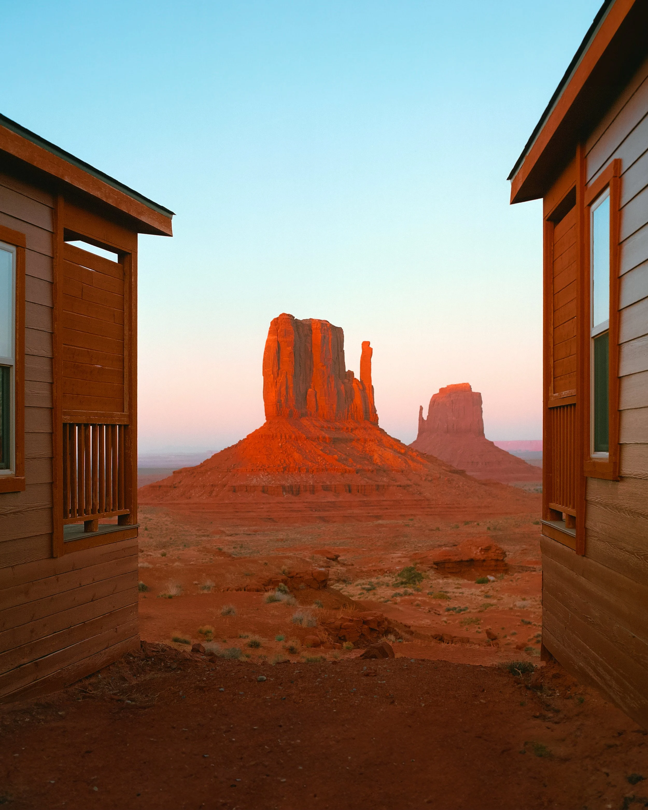 View of iconic red rock formations, Monument Valley, seen from between two wooden houses at sunset.