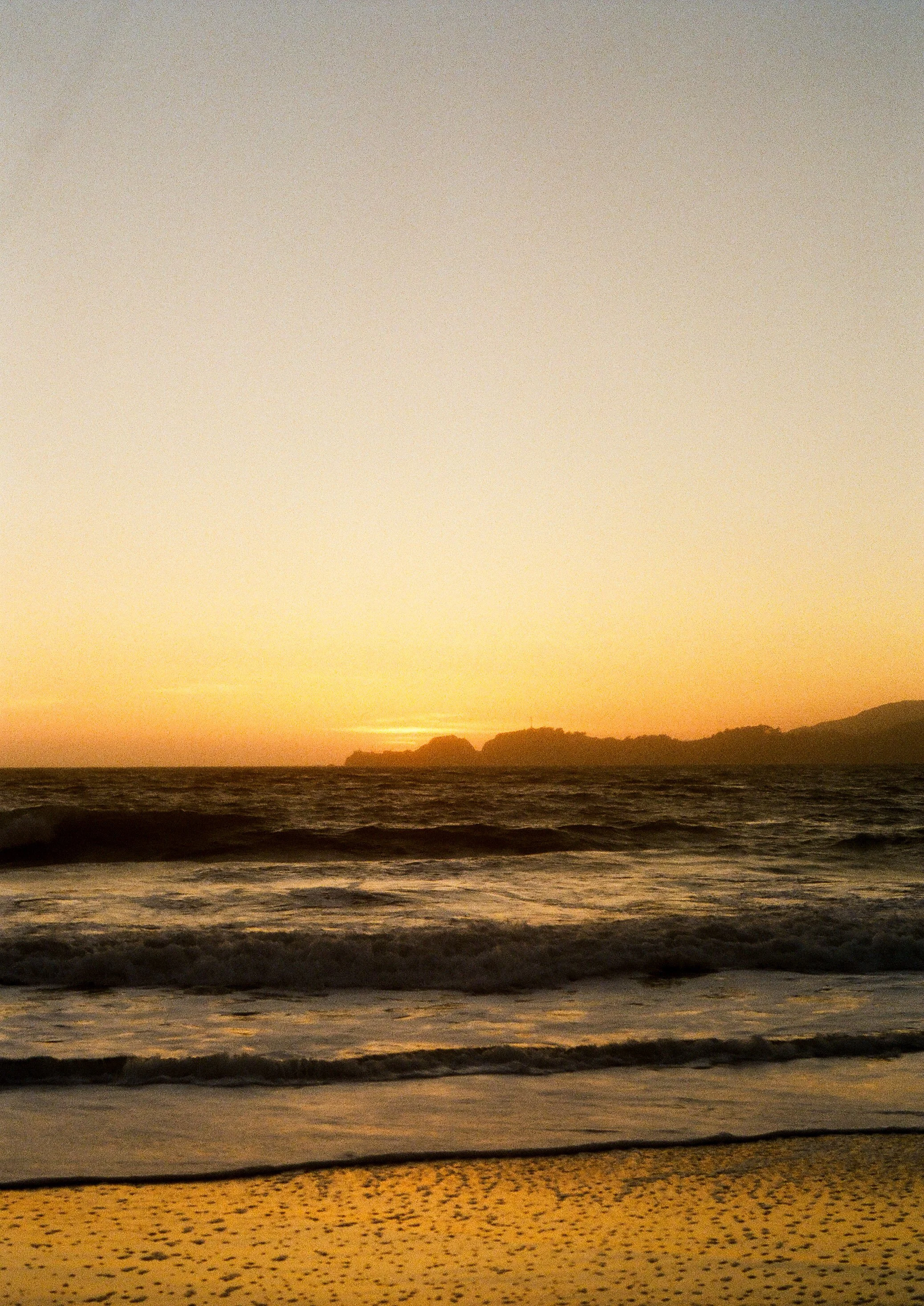 Sunset over the ocean with a distant landmass and gentle waves.