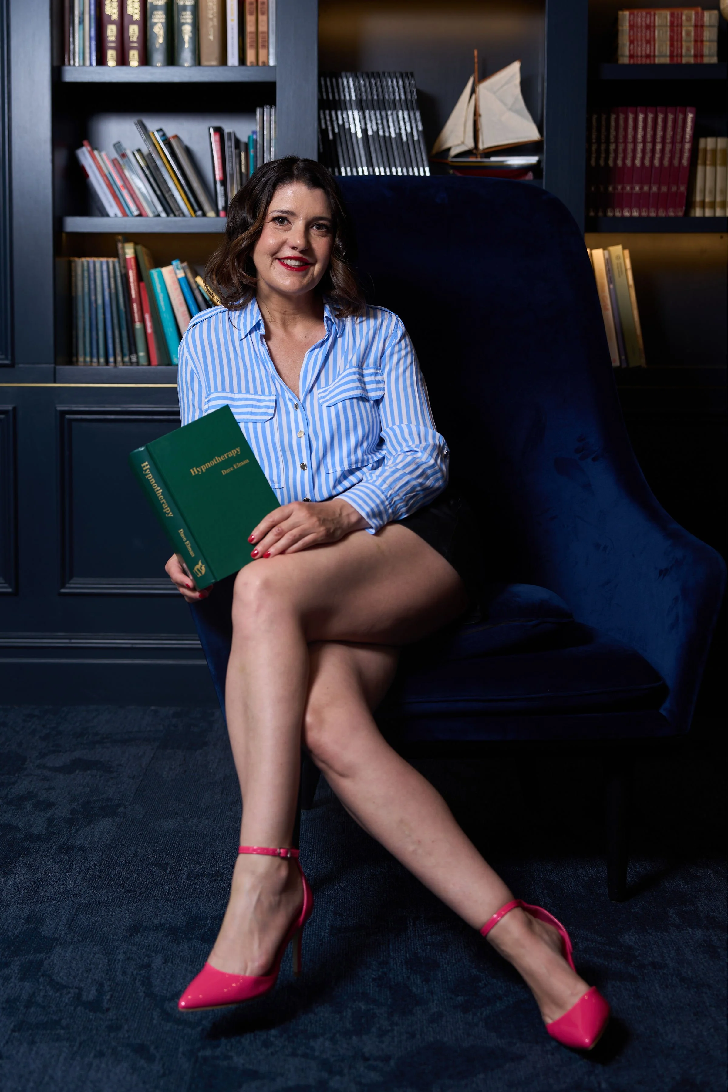 Sabine Lehner clinical hypnotherapist Sydney seated in library holding hypnotherapy book