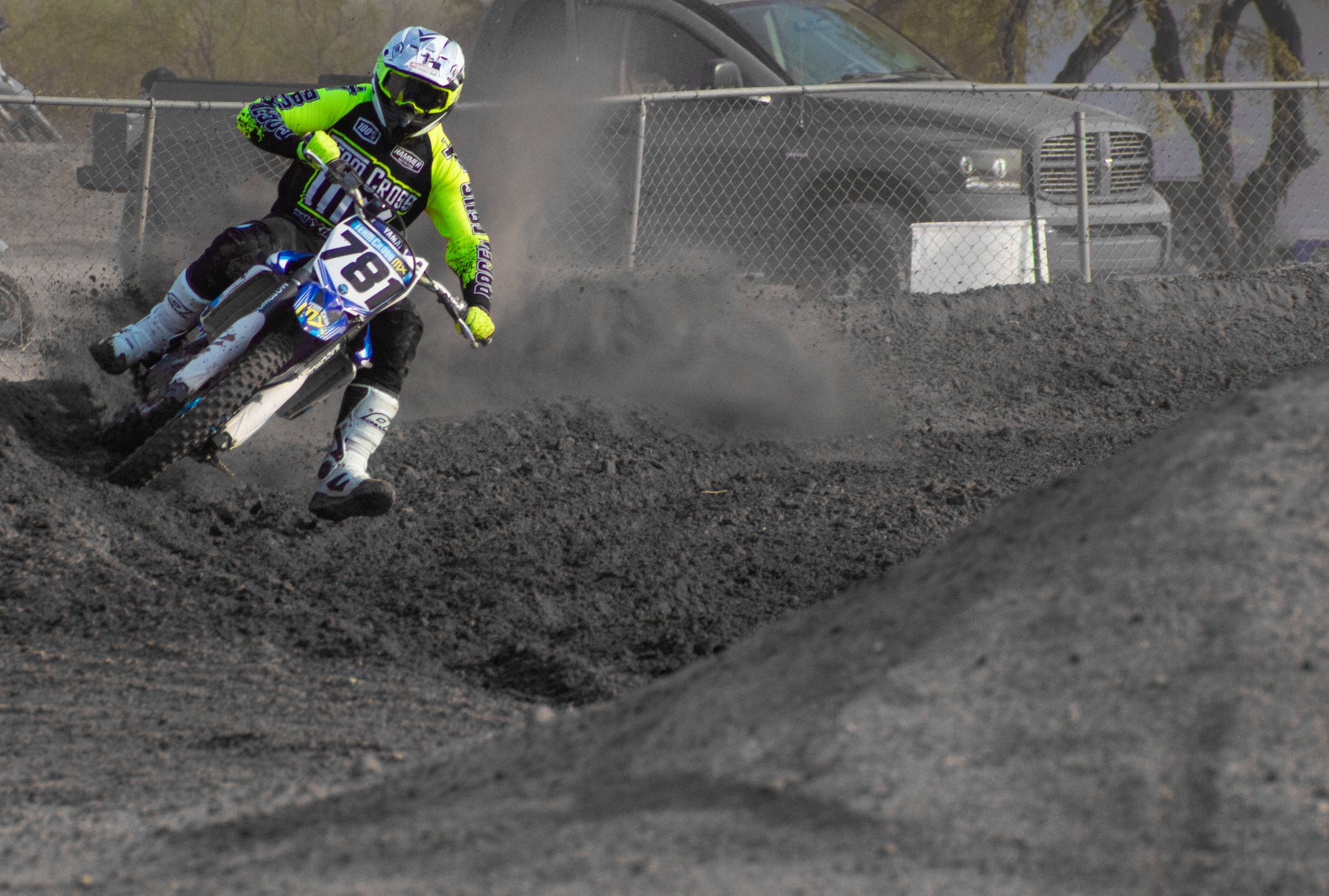 A motocross rider in neon green and black gear on a blue dirt bike, number 761, racing on a dirt track, kicking up dust.