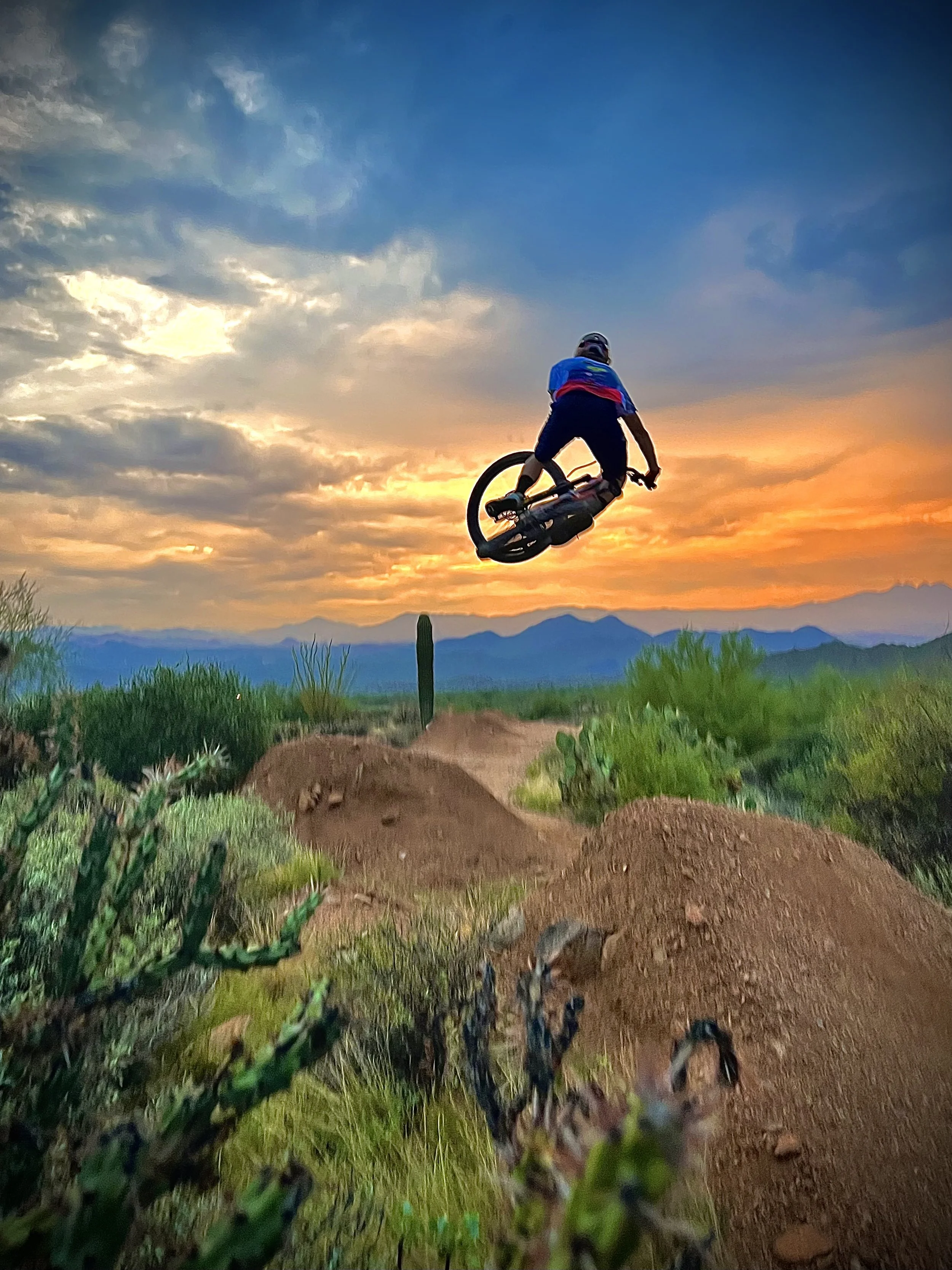 A person performing a BMX jump in a desert landscape at sunset with mountains in the background.