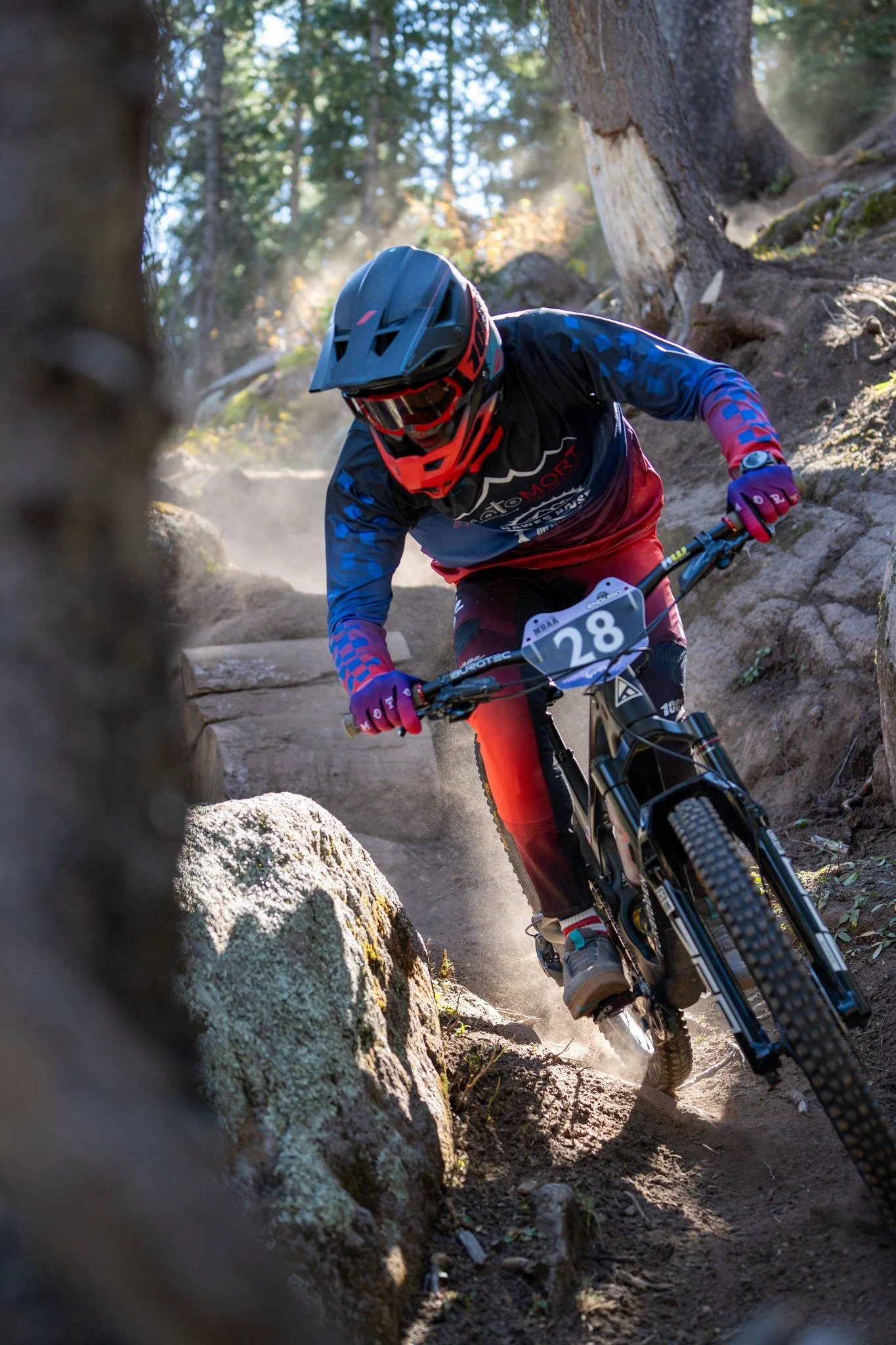 A mountain biker wearing a helmet and goggles navigating a rocky, wooded trail.
