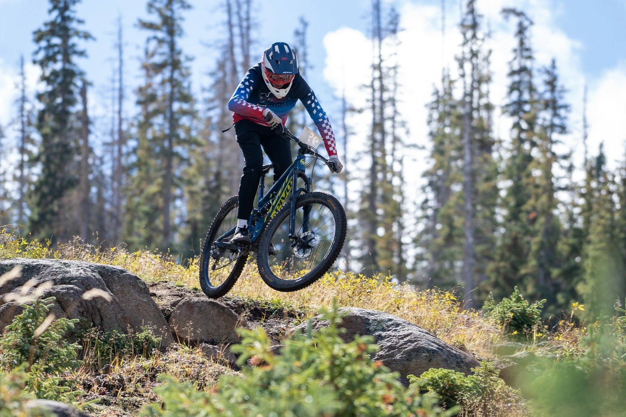Mountain biker jumping off rocks on a trail in a forested area.