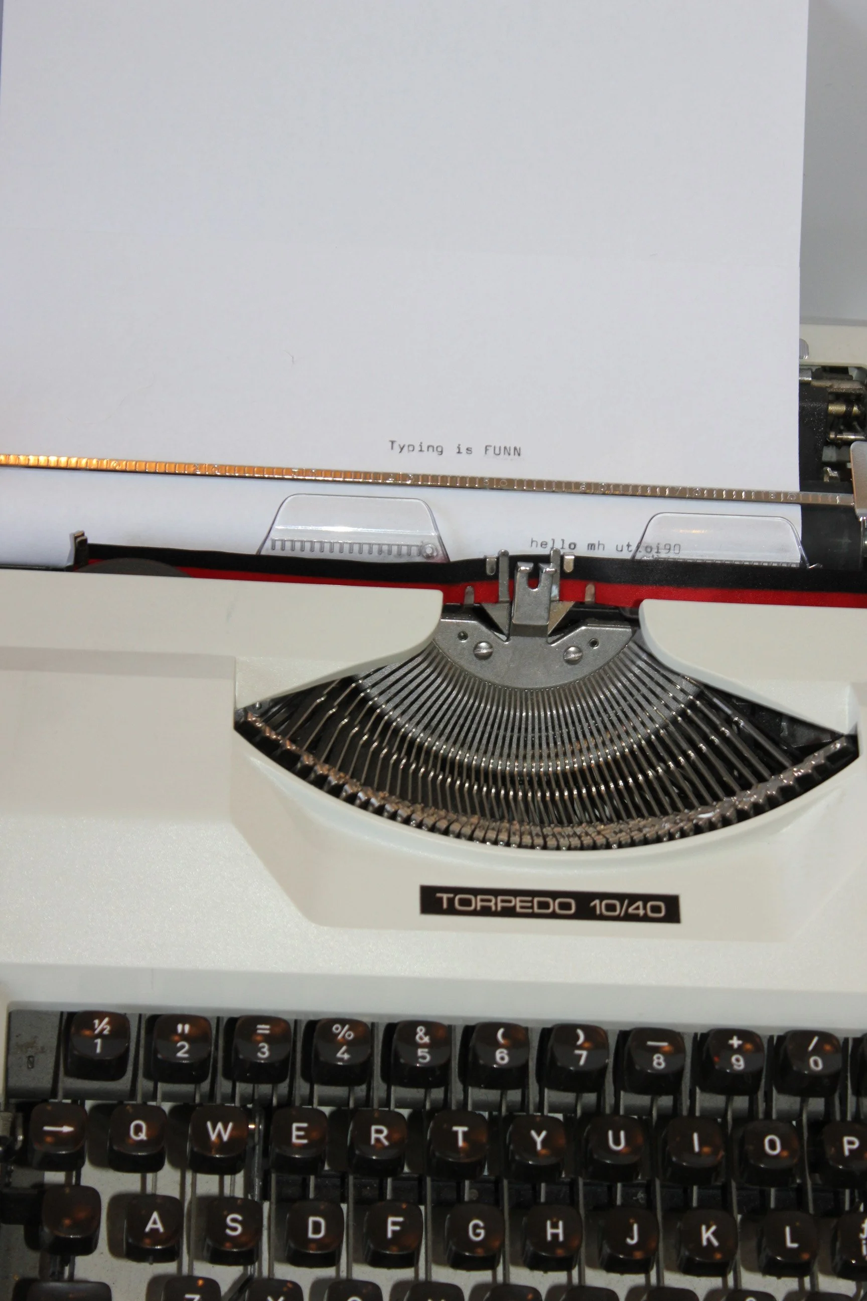A vintage typewriter with the message 'Typing is FUNN' on the paper. The typewriter is placed on a desk, with a keyboard visible at the bottom of the image.