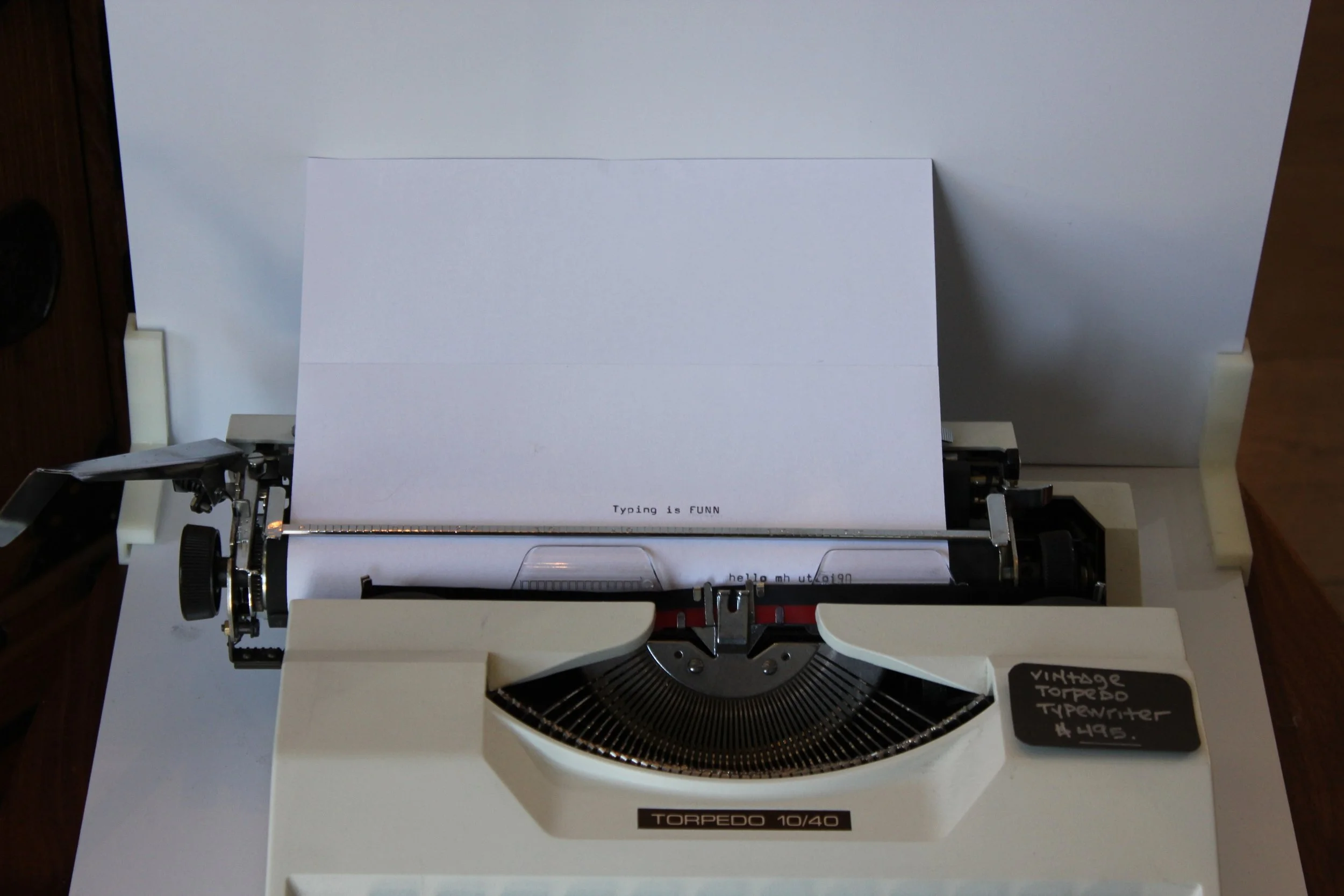 A vintage Torpedo 10/40 typewriter with white paper inserted, centered on a white surface, with small handwritten note indicating the typewriter model and #495.