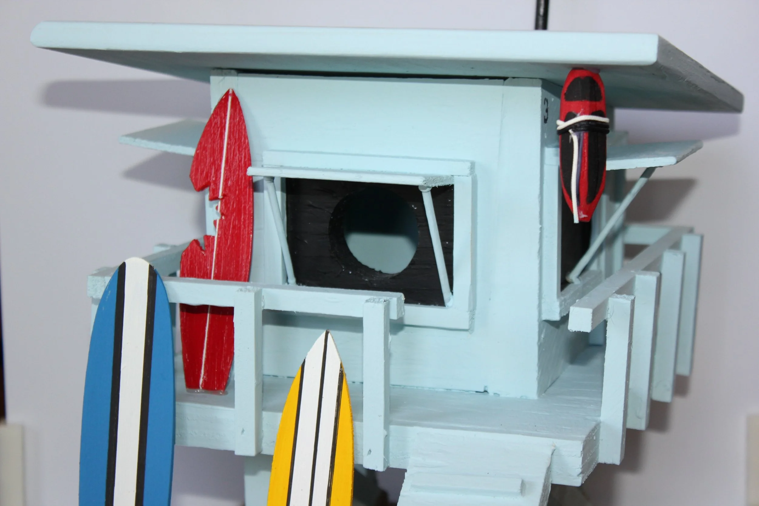 Small white wooden beach house with miniature surfboards hanging on the side, located indoors.