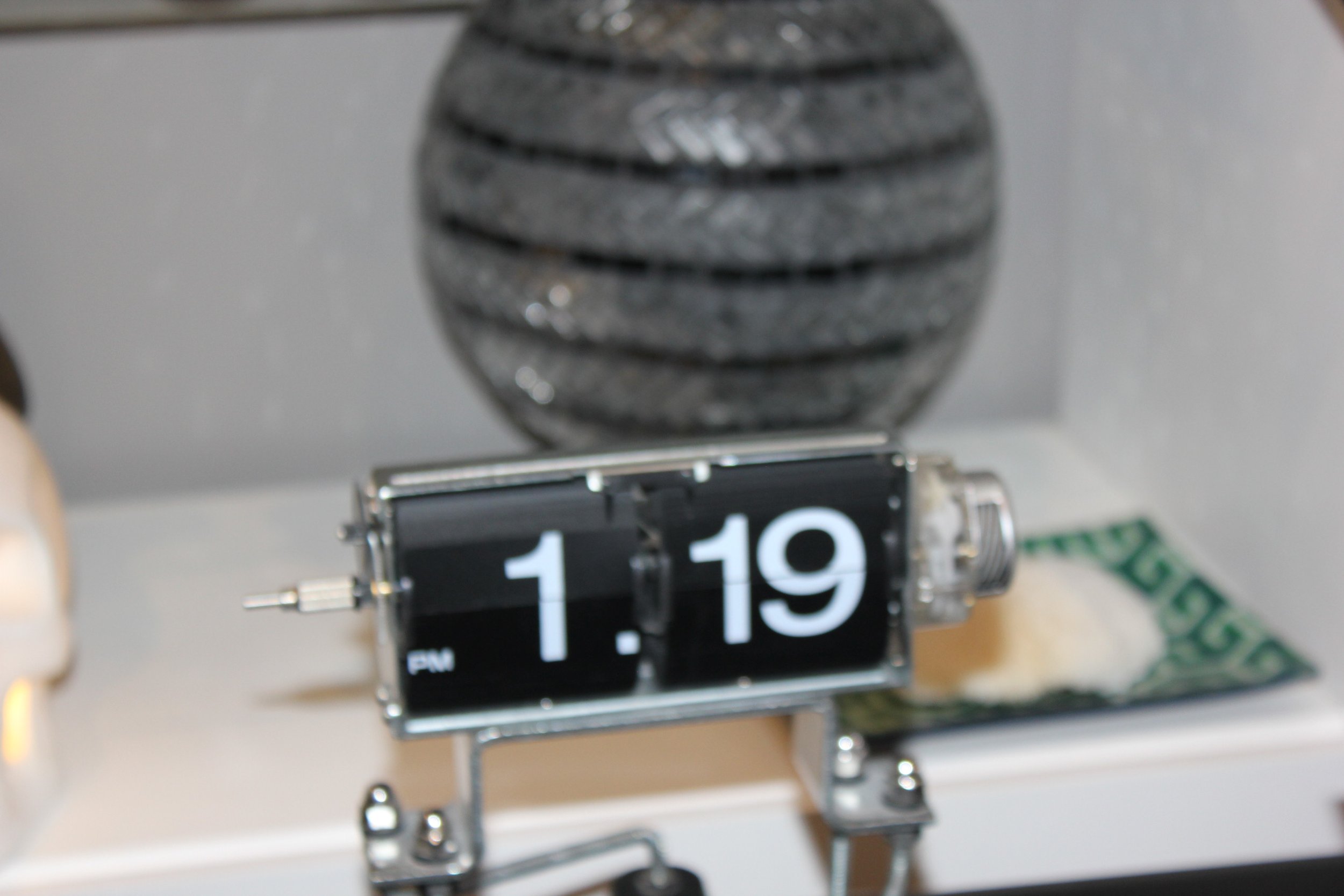 Close-up of a vintage flip clock displaying the time 11:19, placed on a surface with blurred objects in the background.