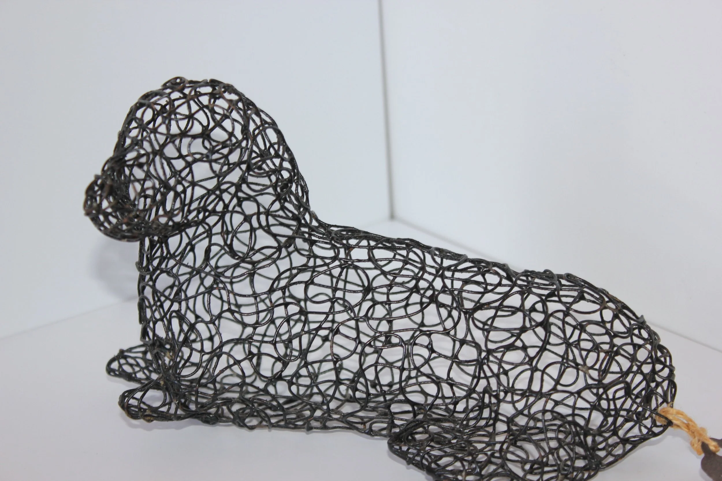A black wire sculpture of a reclining woman with long hair, made from intertwined loops of wire, set against a plain white background.