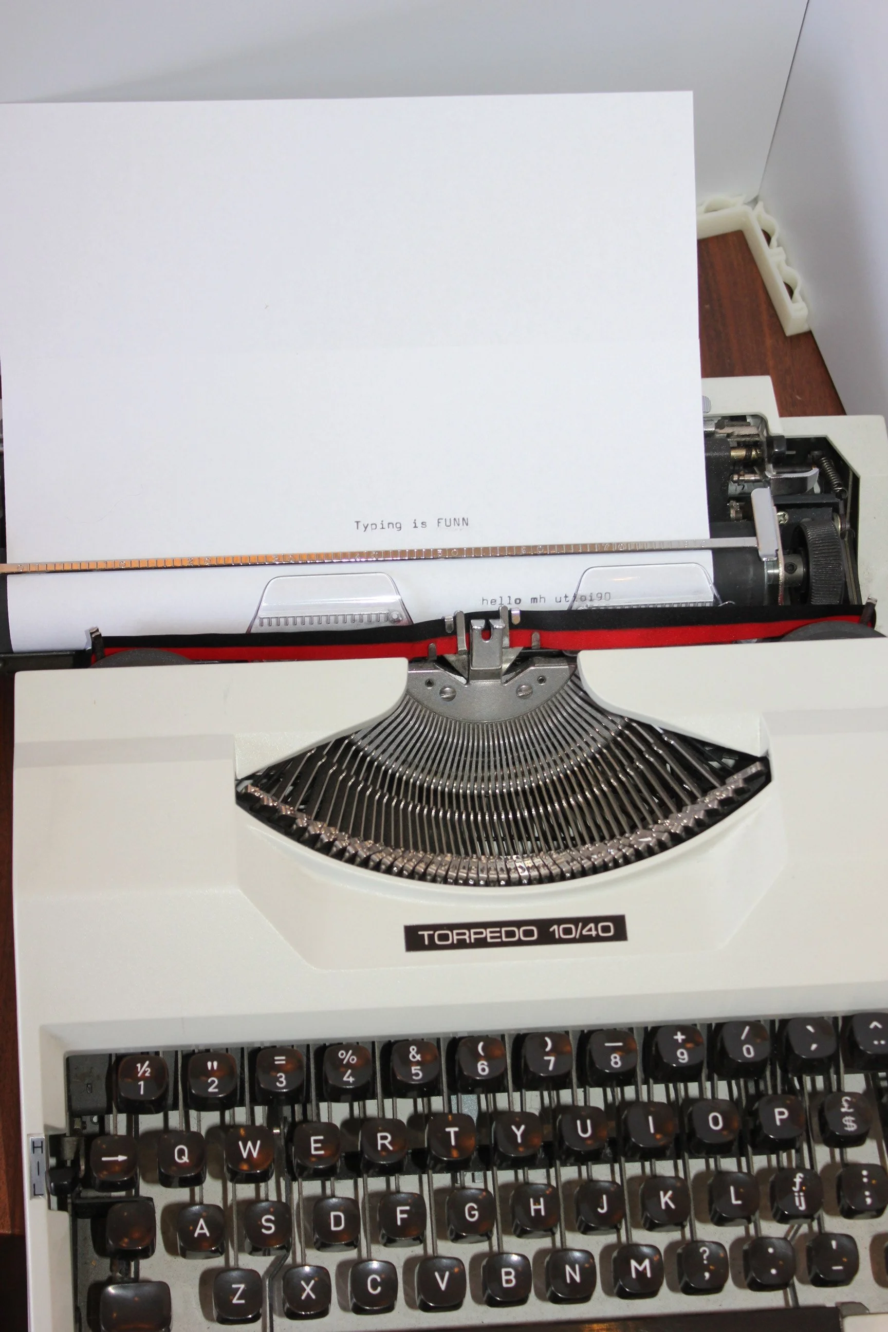 A vintage white typewriter with black keys and a piece of paper inserted, displaying text that reads 'Typing is FUNN' and part of a keyboard below titled 'TORPEDO 10/40'.