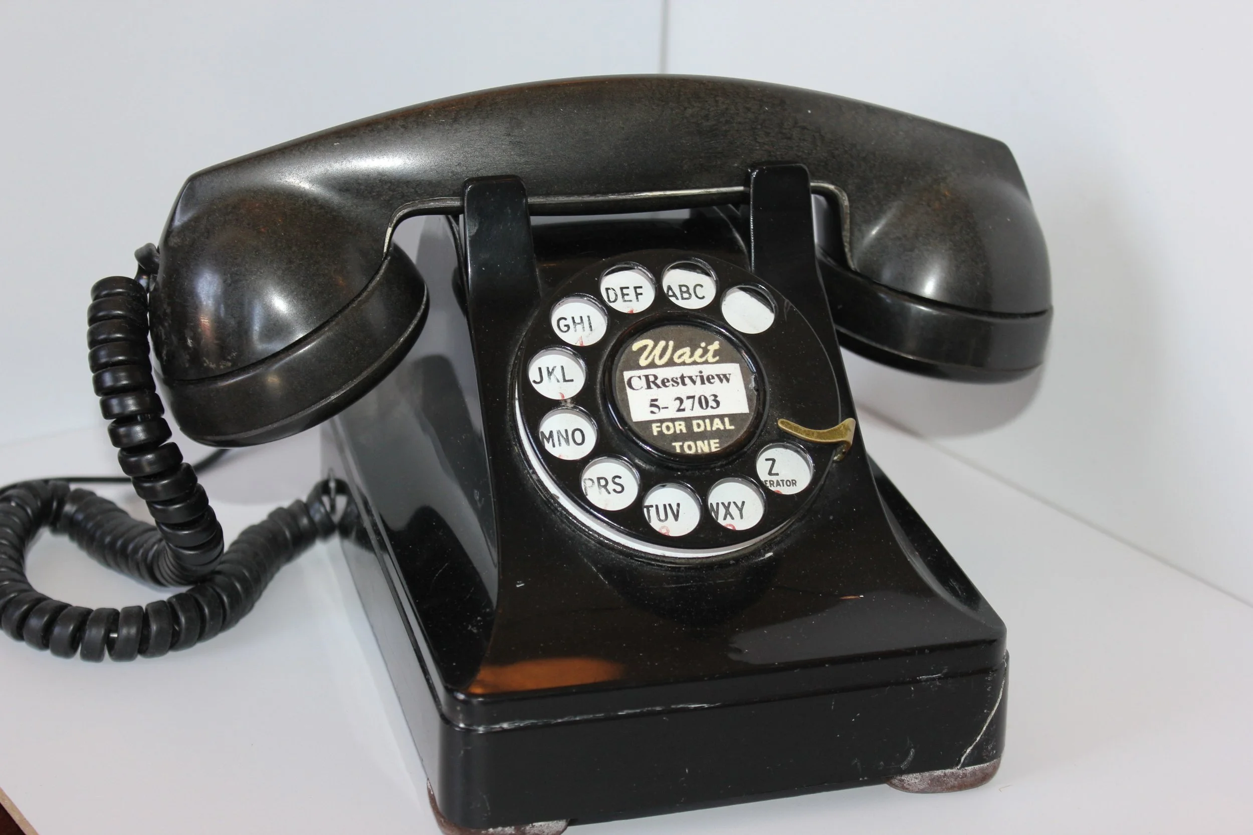 A vintage black rotary telephone with a coiled cord on a white surface.