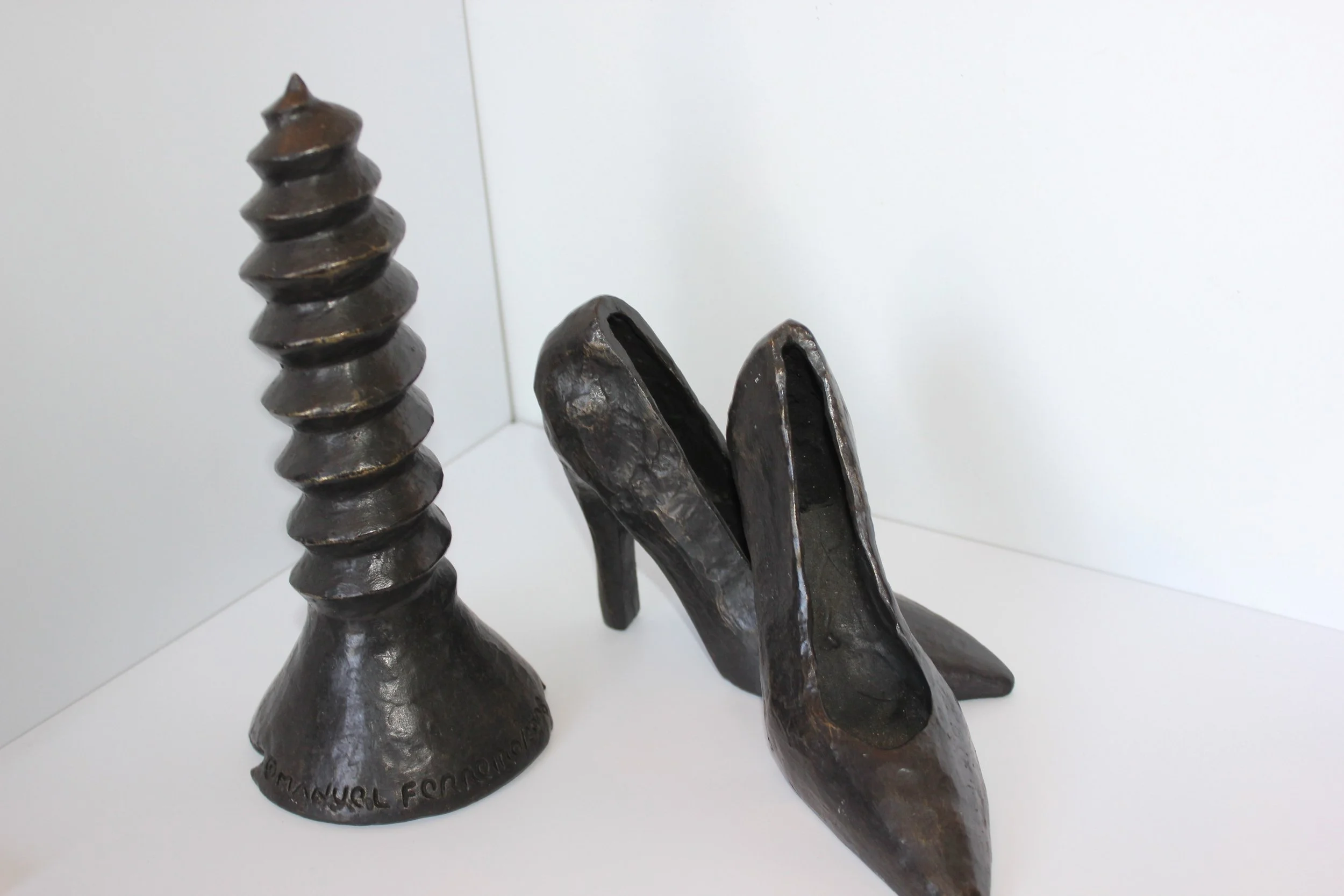 A collection of dark metal sculptures resembling abstract shapes, including a spiral, a pair of elongated shapes, and a bell-shaped object with engraved text.