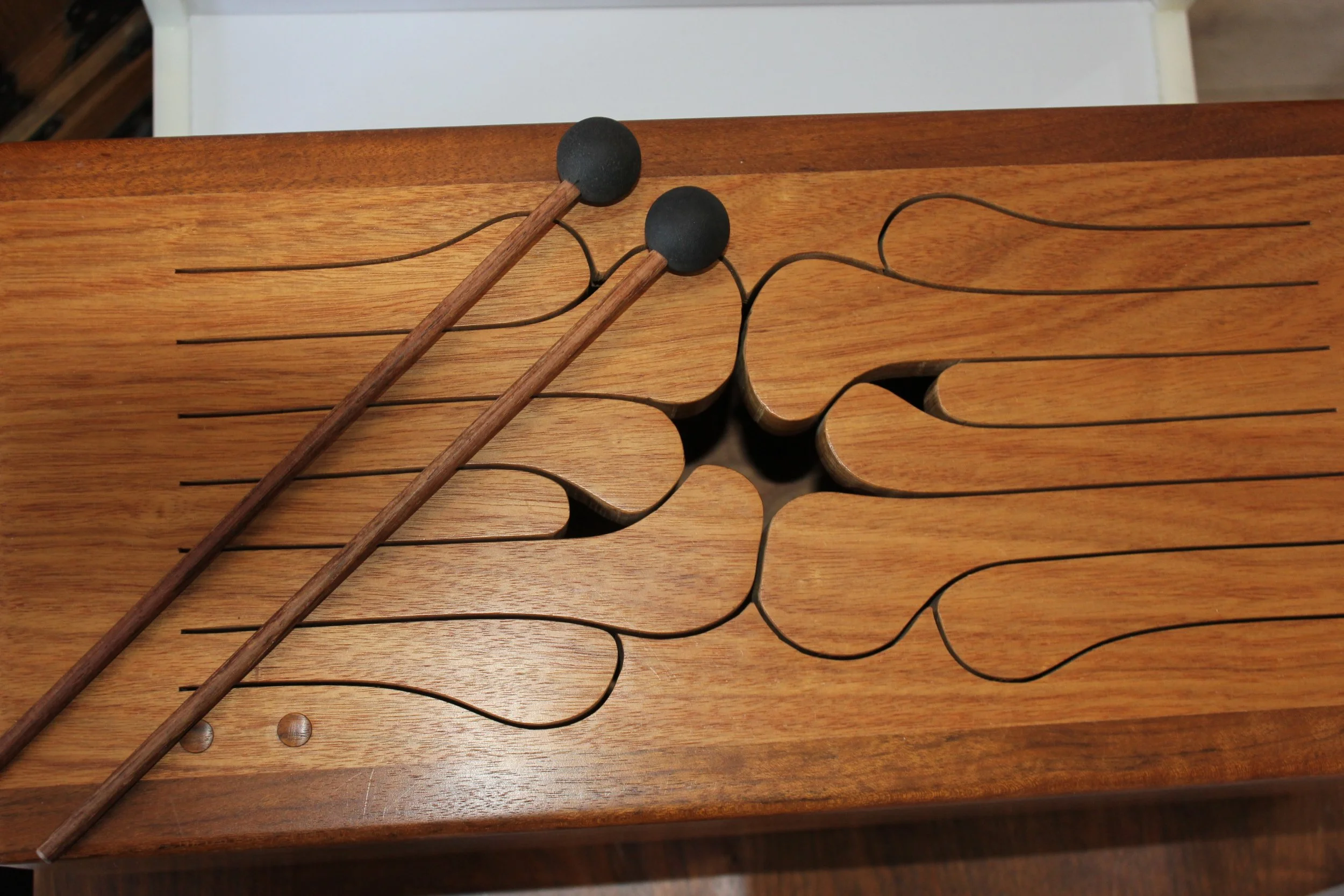 A wooden percussion instrument with metal wires and black mallets resting on it.