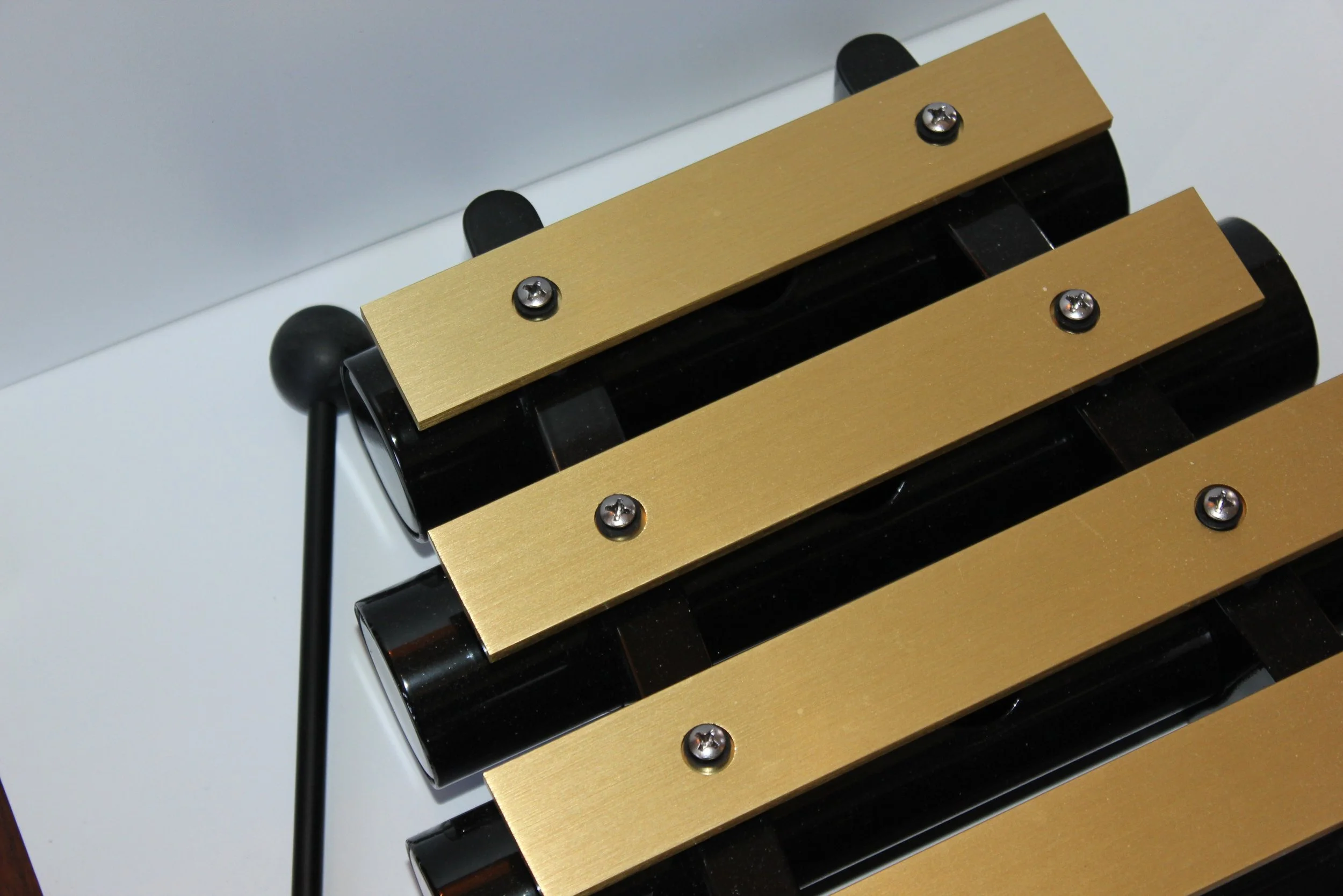 Close-up of a xylophone with golden metal bars, black frame, and black mallets over a white background.