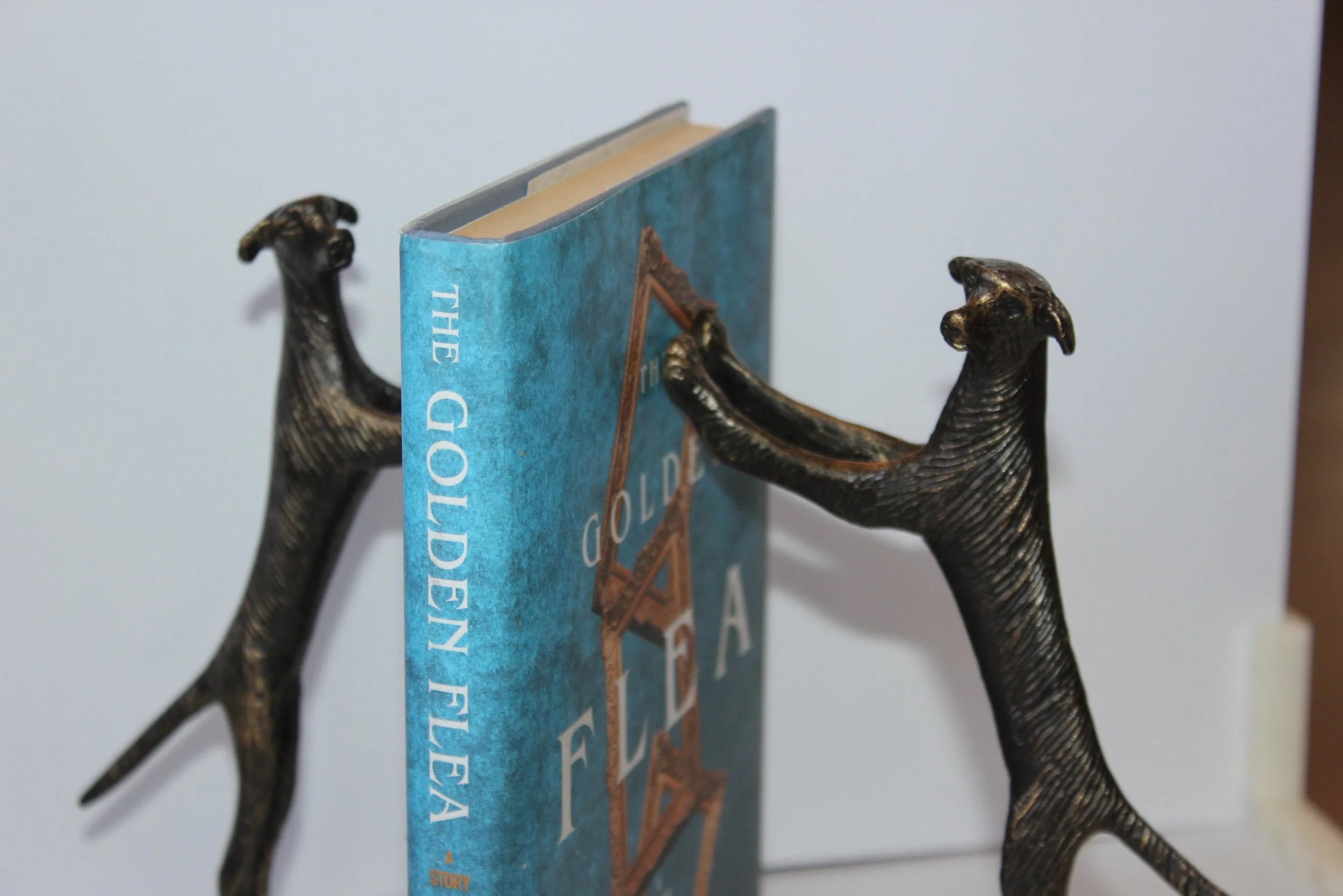 Two dragon figurines holding a blue paperback book titled 'The Golden Fleece' against a plain white background.