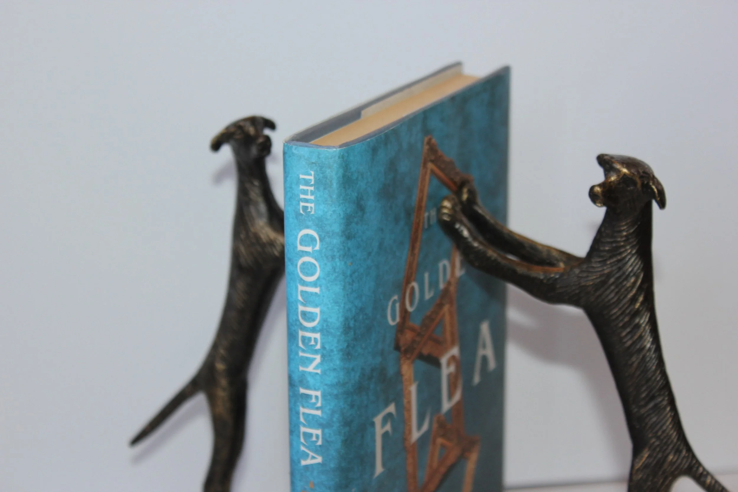 Close-up of two bronze bear bookends holding a blue book with the title partially visible, set against a plain background.