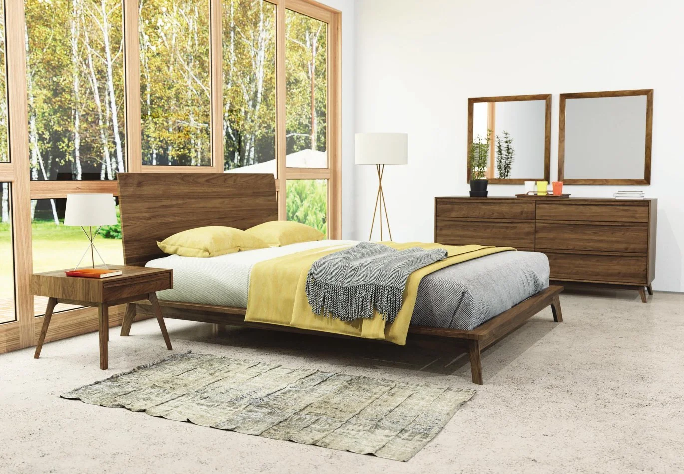 A modern bedroom with a large wooden bed, yellow pillows, a yellow blanket, and a gray throw. There is a wooden nightstand with a white lamp and a book, a textured area rug, and a tall white lamp. The room features large windows with a view of trees and greenery, and a wooden dresser with two framed mirrors, potted plants, and books.