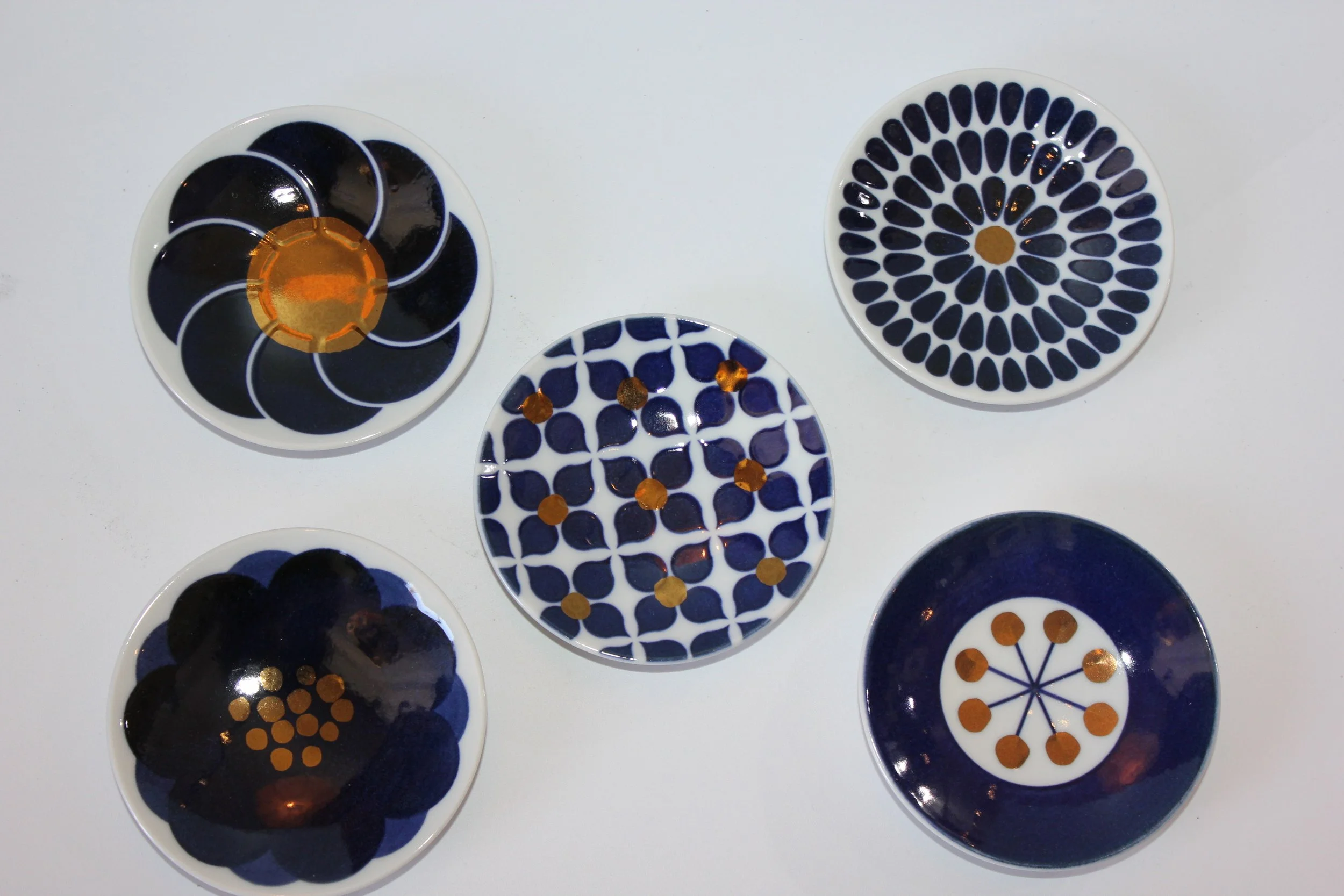 Set of small decorative plates with blue, black, and white geometric and floral patterns, some featuring orange or gold accents.