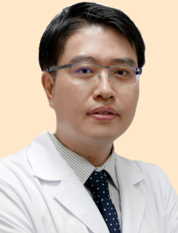A man with glasses in a white coat and a dark blue tie, standing against a plain background.
