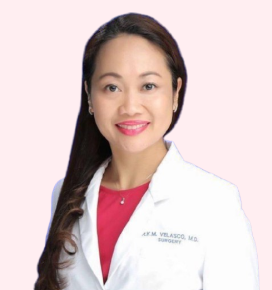 A woman with long dark hair wearing a white medical coat and red top, smiling against a light pink background.