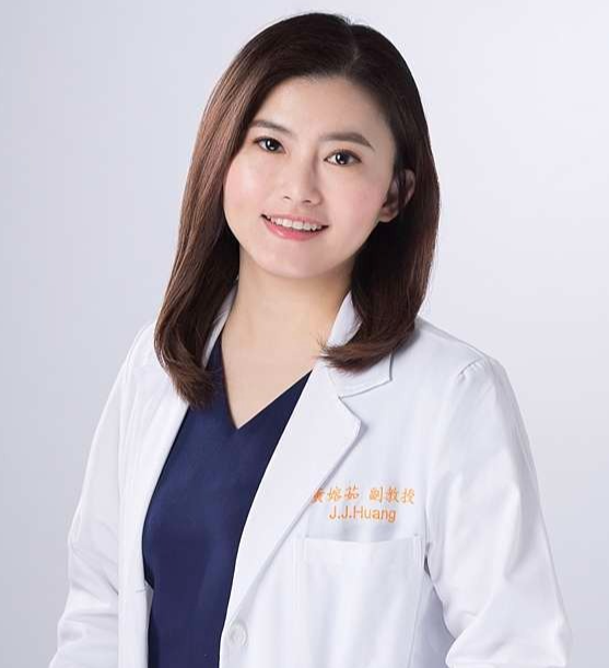 A woman with shoulder-length brown hair wearing a white medical coat and navy blue scrubs smiling against a light gray background.