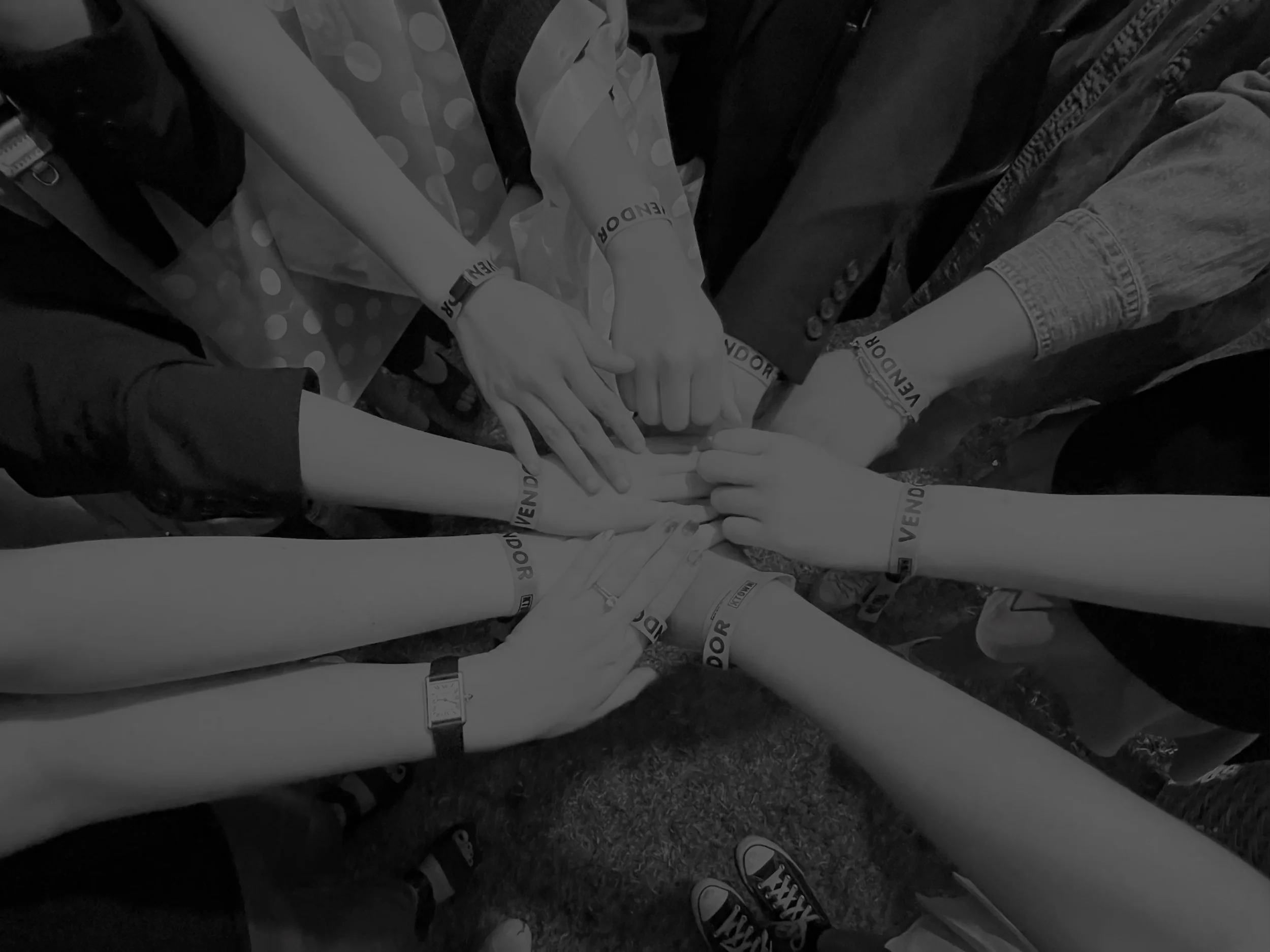 Multiple people with outstretched hands reaching towards a central point, wearing wristbands that have
