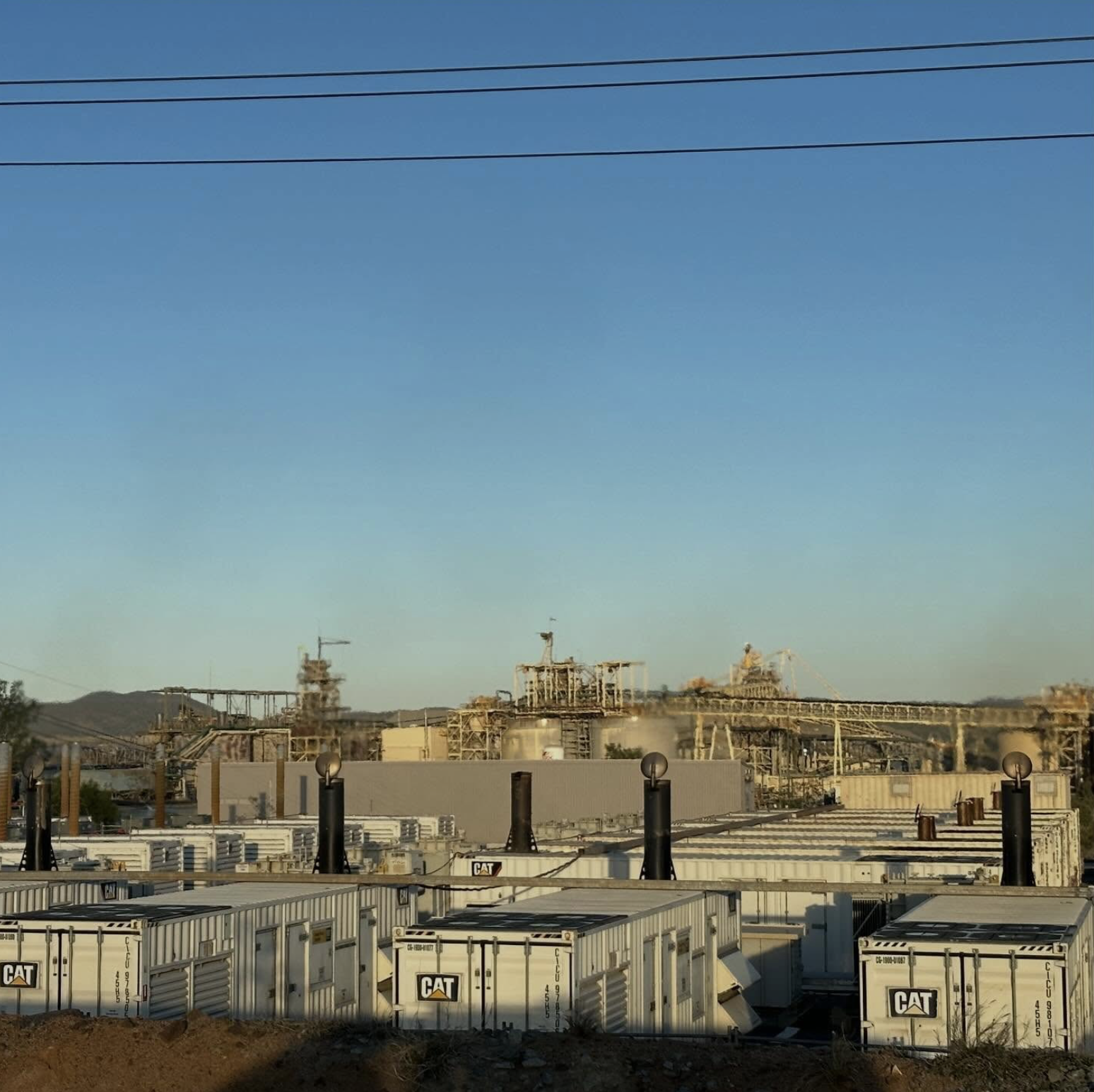 Industrial site with electric generators, equipment, and structures under a clear blue sky.