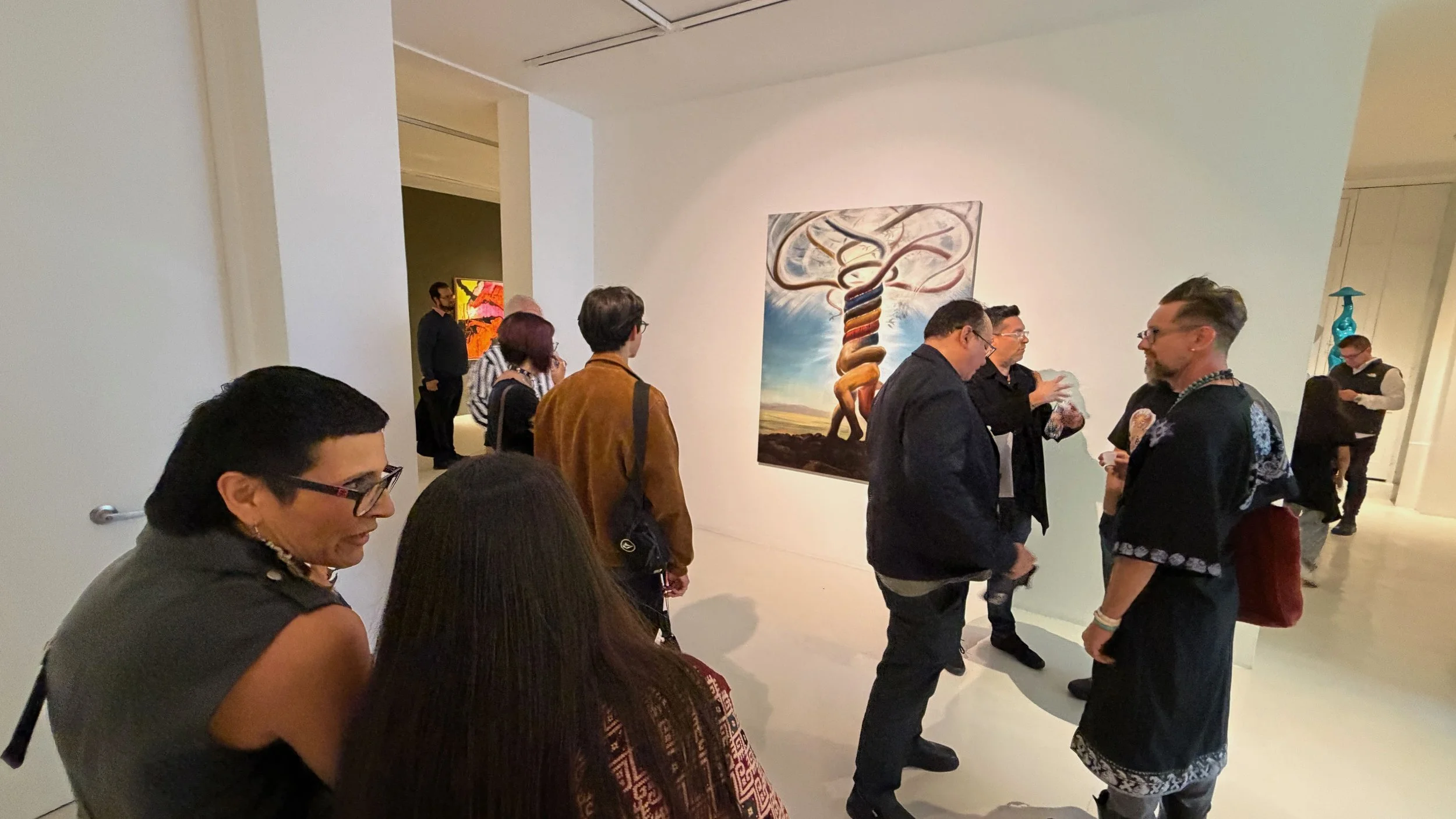 People gathered in an art gallery viewing paintings on the wall.