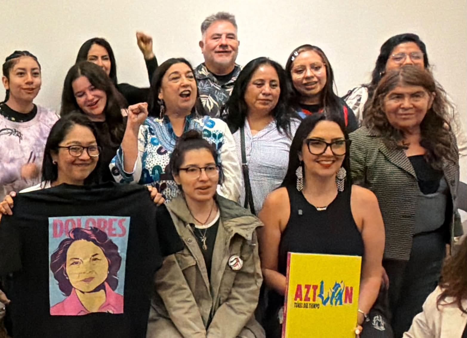 Group of women gathered together, some holding signs, smiling and celebrating.