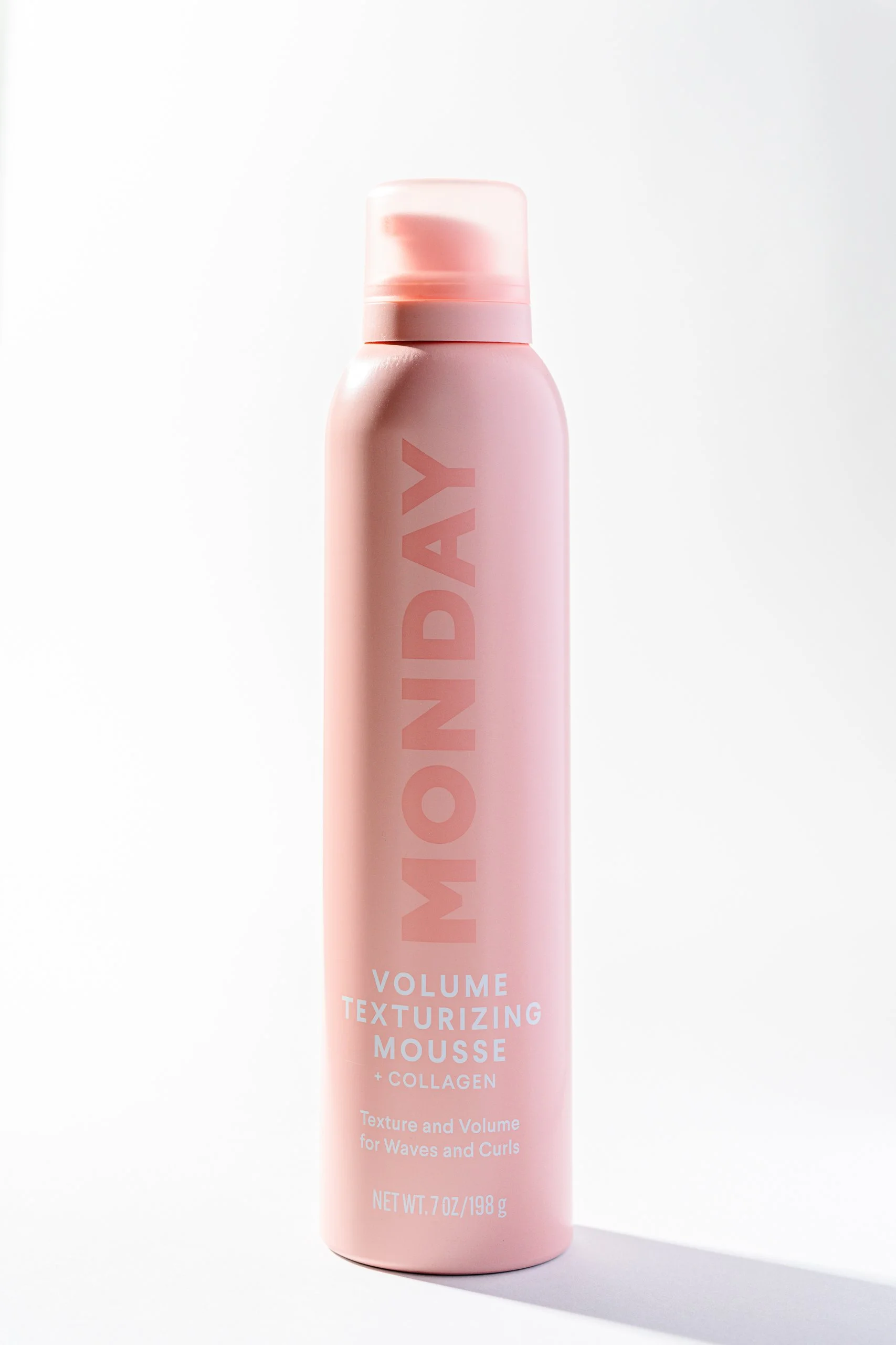Pink bottle of volumizing texturizing mousse with collagen on a white background, casting a shadow.
