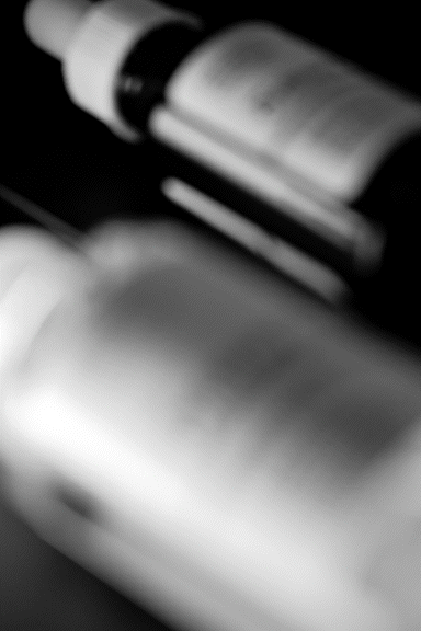 A close-up black and white image of bottles from The Ordinary, lying on a dark surface.