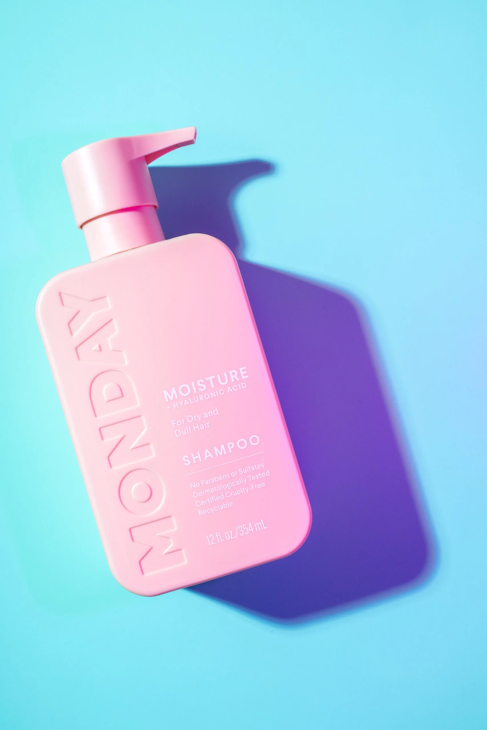 Pink bottle of MONDAY Moisture Shampoo for dry and dull hair on a blue background with a shadow.