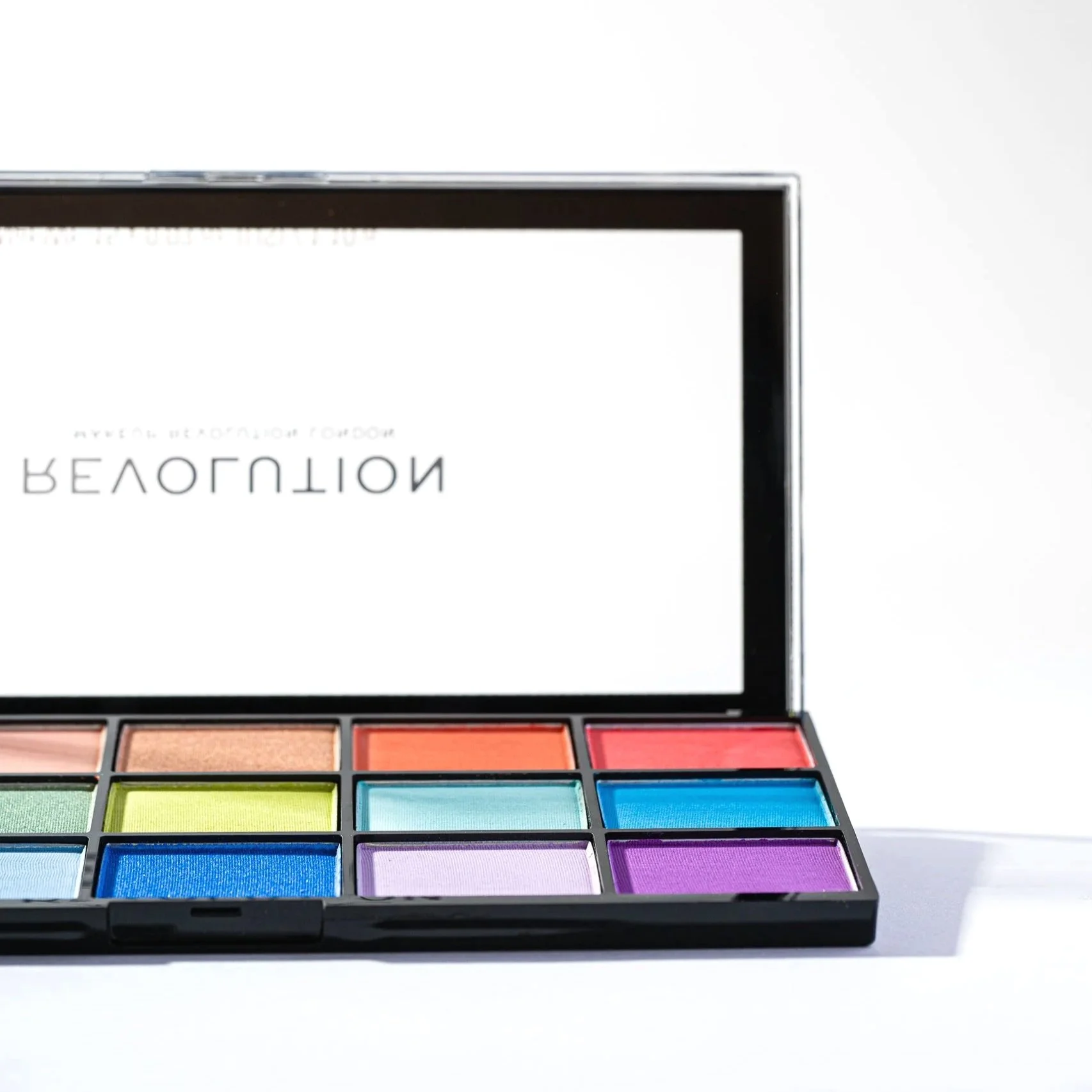 Open colorful eyeshadow palette with multiple shades arranged in rows on a white background.