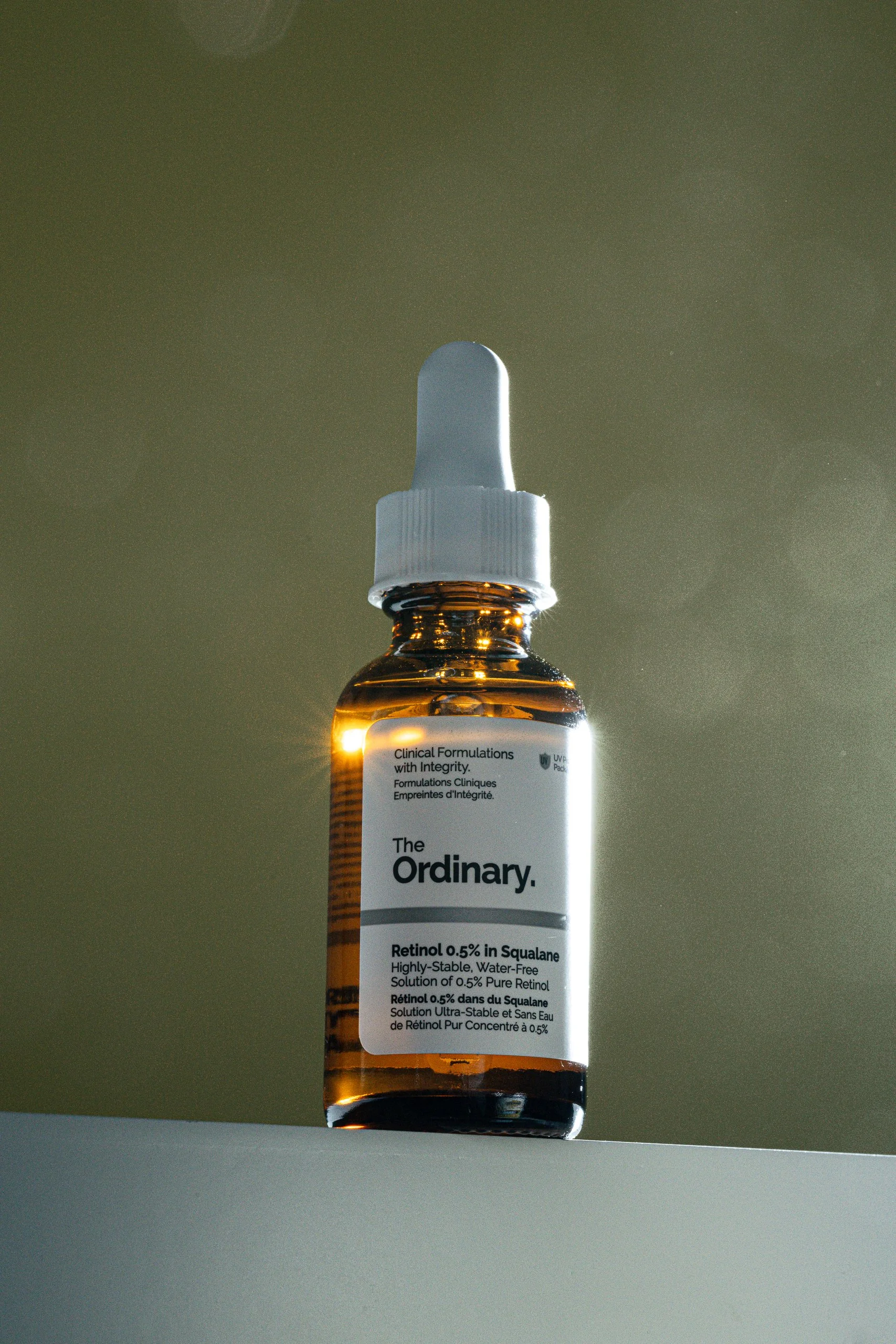 A small brown glass bottle with a white dropper cap, containing Retinol 0.5% in Squalane, with a partially visible label displaying text in English and French.